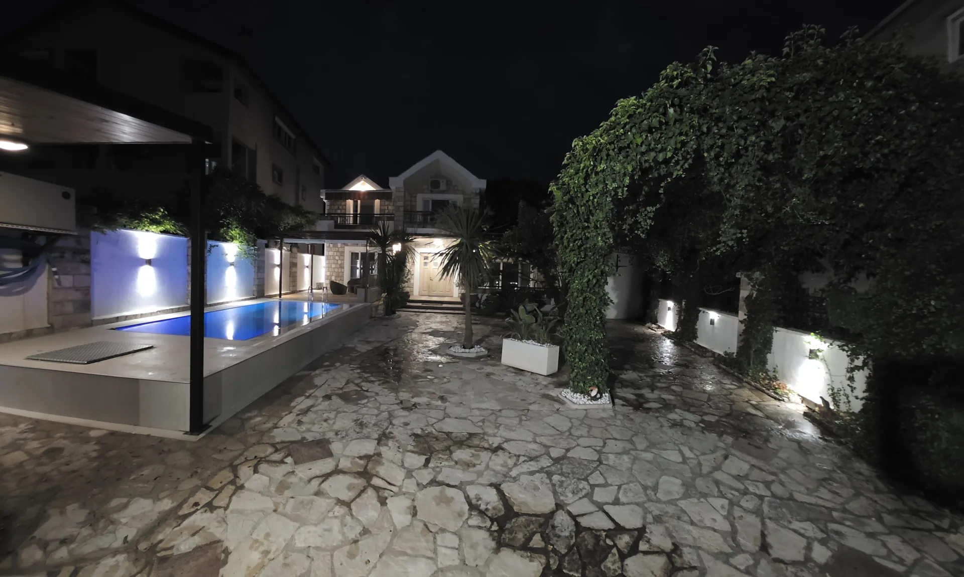 Nachtansicht eines beleuchteten Pools mit Steinhof und grüner Bogen.