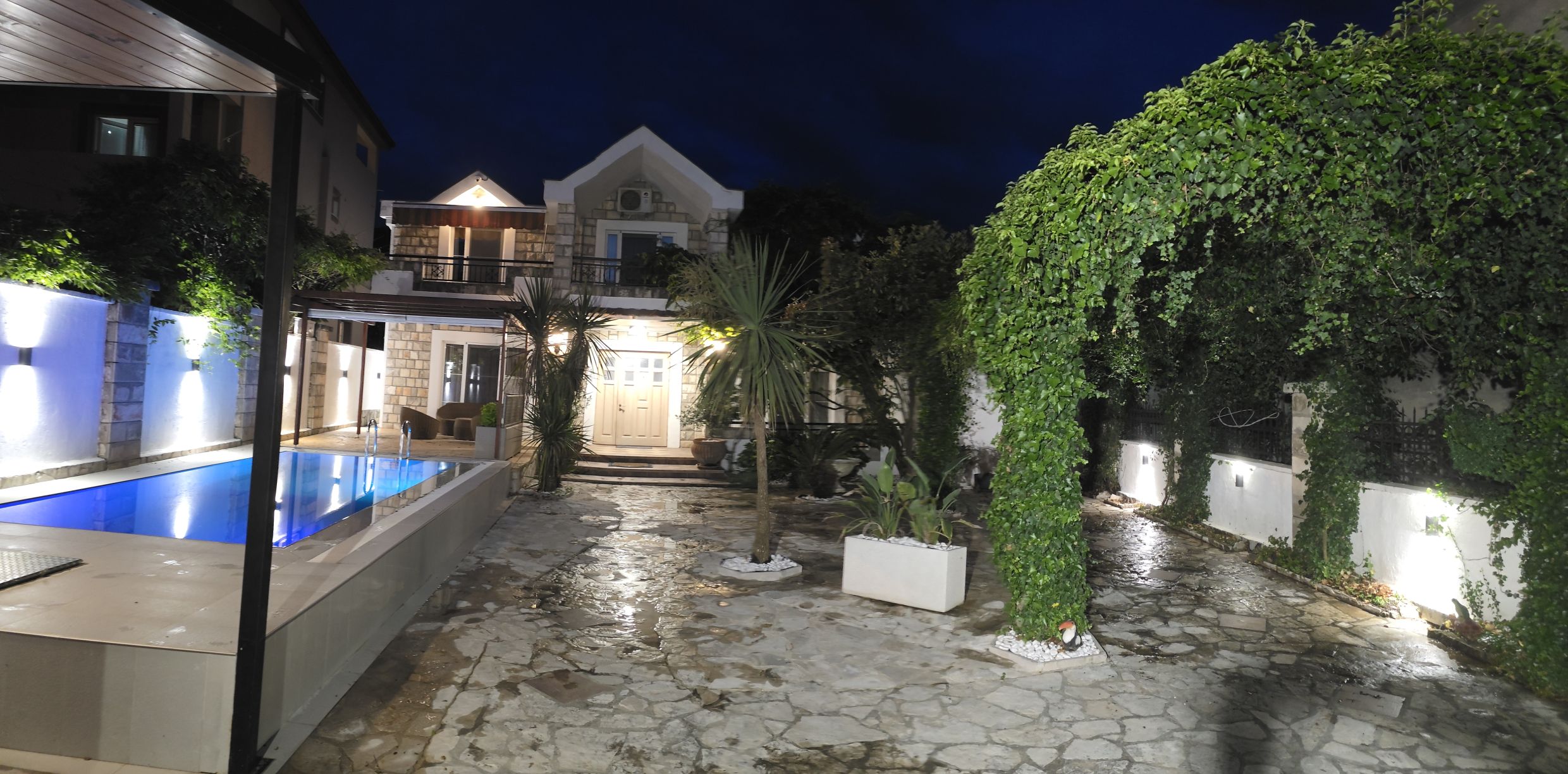Maison à deux étages à Tivat, Monténégro, avec piscine, terrasse en pierre, aménagement paysager et éclairage nocturne.