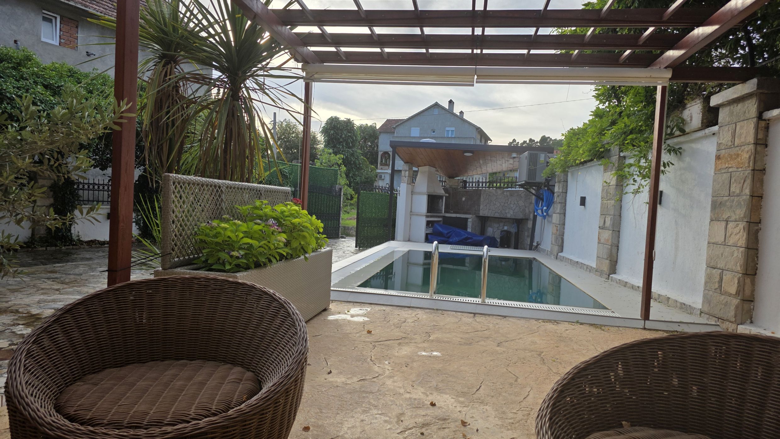 Terrasse avec piscine et espace barbecue dans une maison privée à Tivat, Monténégro : mobilier en osier et vue sur le jardin.