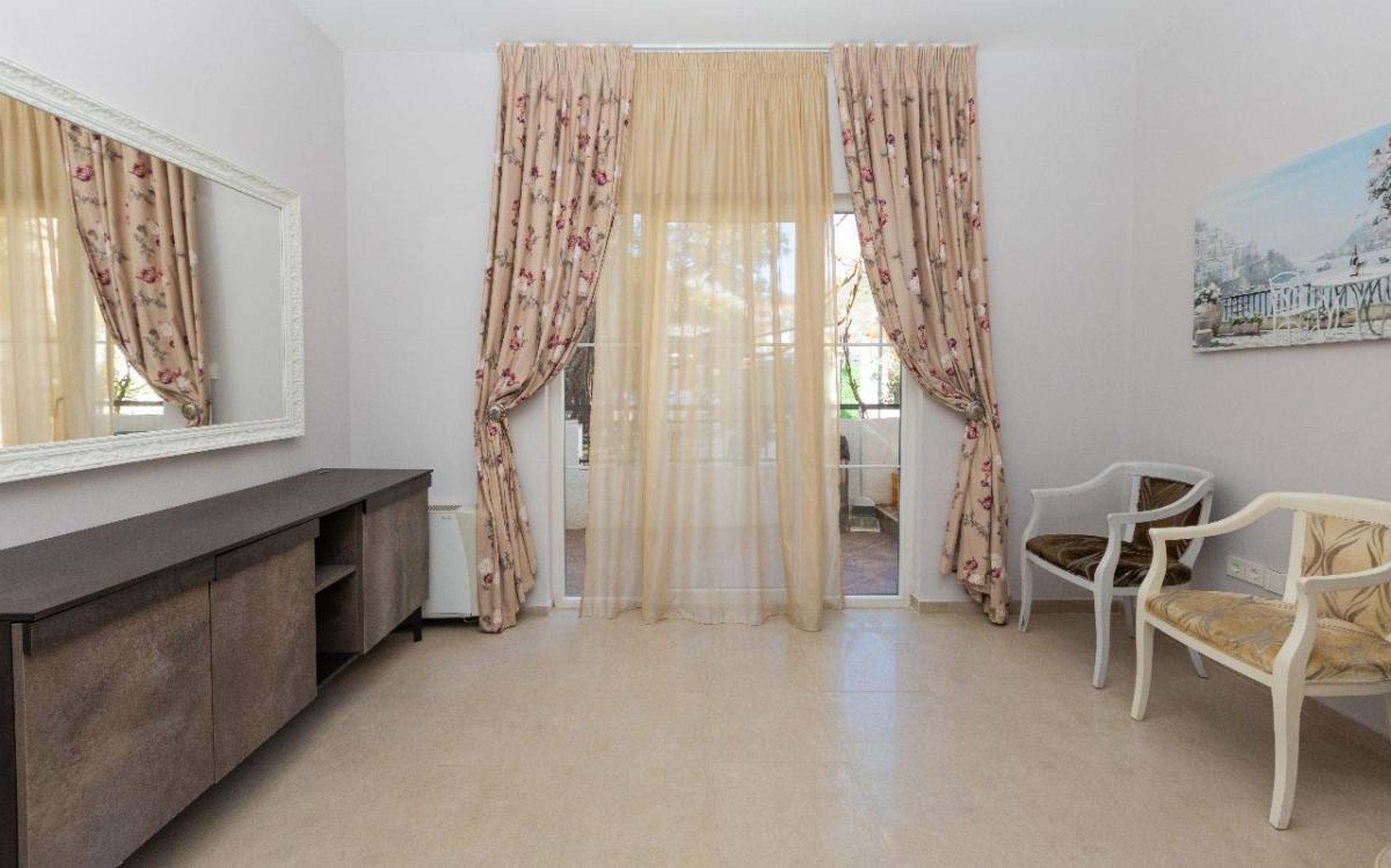 Salon lumineux dans une maison à Tivat, Monténégro : miroir dans un cadre blanc, chaises classiques et accès à la terrasse.