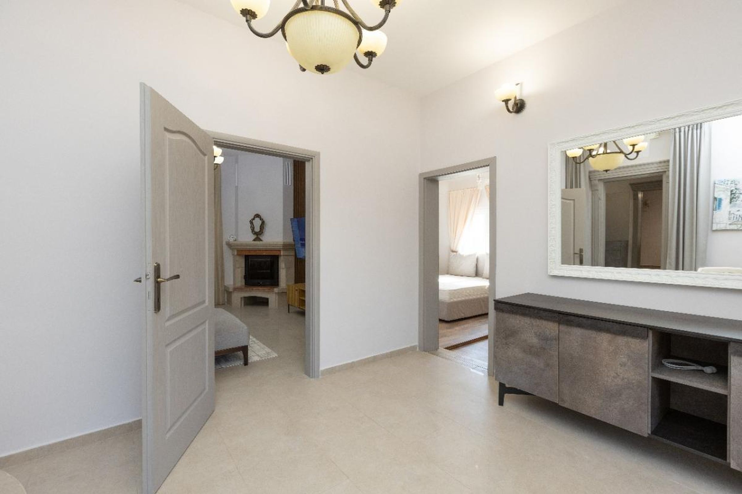 Hall lumineux avec commode et miroir dans une maison à Tivat, Monténégro, vue sur le salon avec cheminée et la chambre.