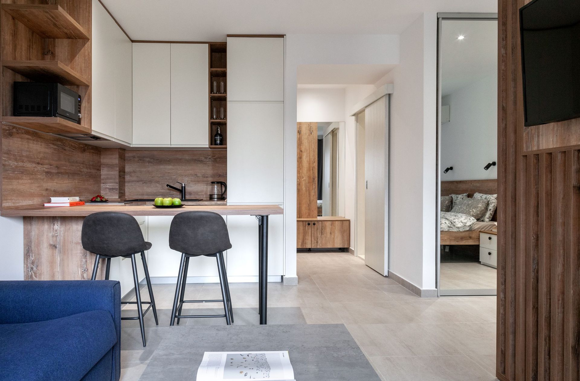 Moderne Wohnküche mit Bar in einer Wohnung in Kotor, Montenegro: helle Möbel, Holz und Blick ins Schlafzimmer.