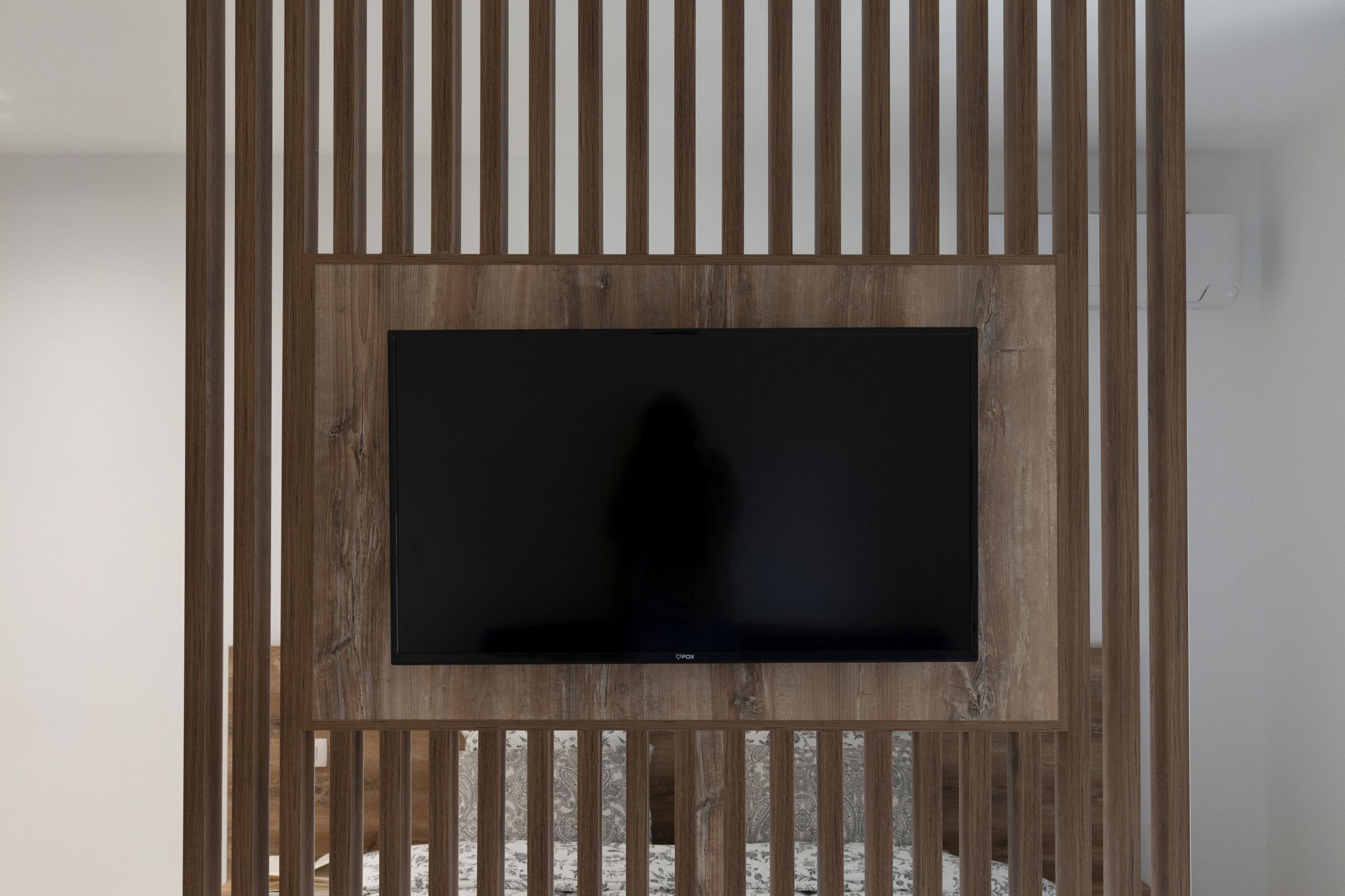 Modernes Schlafzimmer in einer Wohnung in Kotor, Montenegro: Fernseher an einer dekorativen Holztrennwand mit Lamellen.