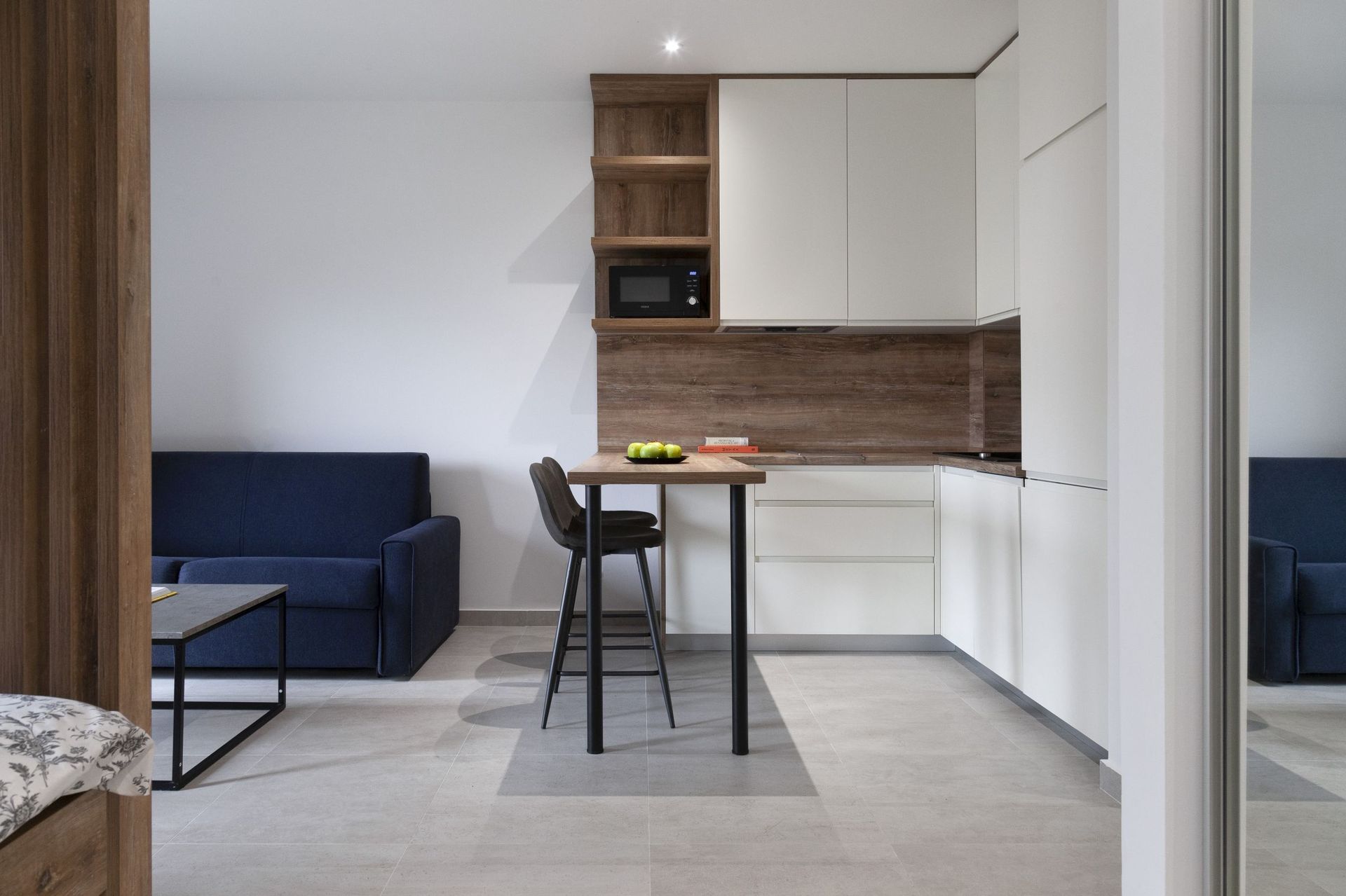 Moderne Wohnküche in einer Wohnung in Kotor, Montenegro: weiße Fronten, Bartheke und blaues Sofa im Interieur.