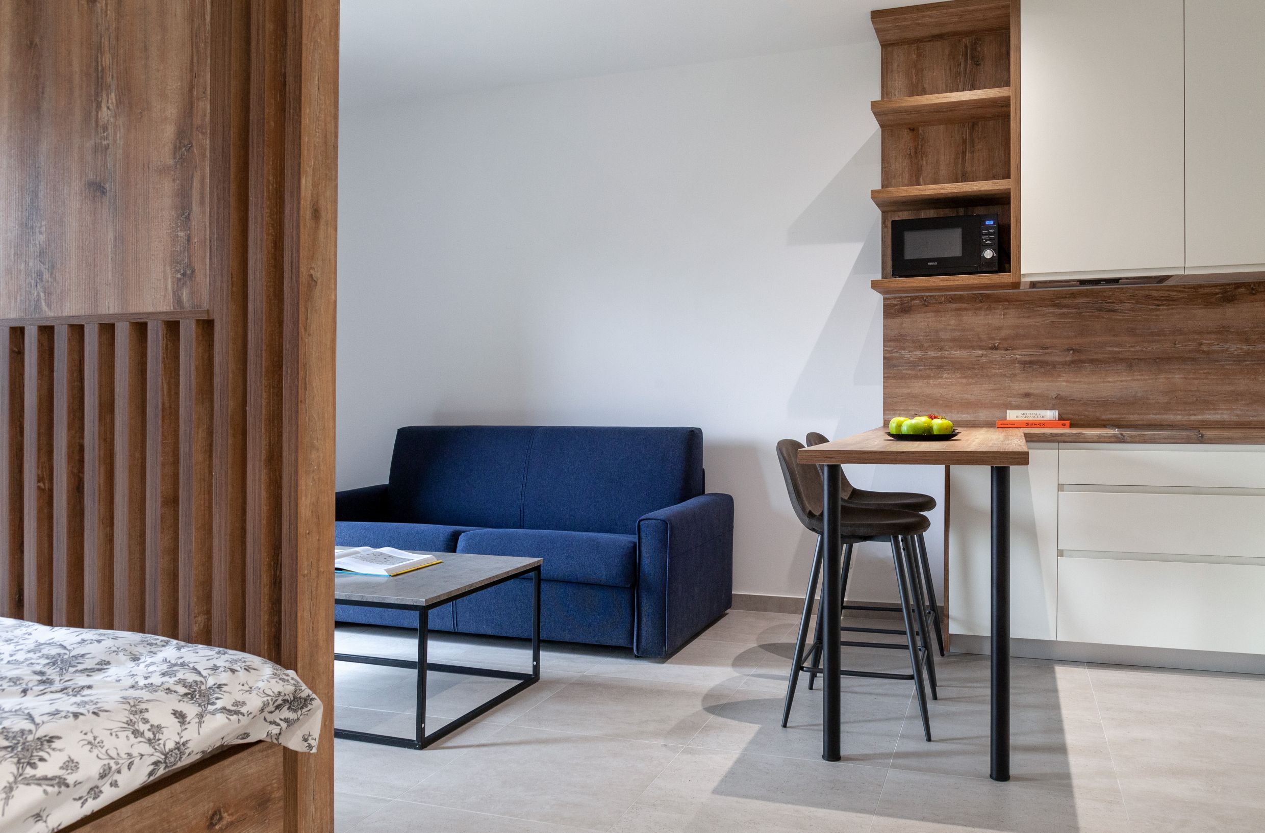 Modernes Wohnzimmer mit blauem Sofa und Küche in einer Wohnung in Kotor, Montenegro: stilvolles Interieur mit Holzverkleidung.