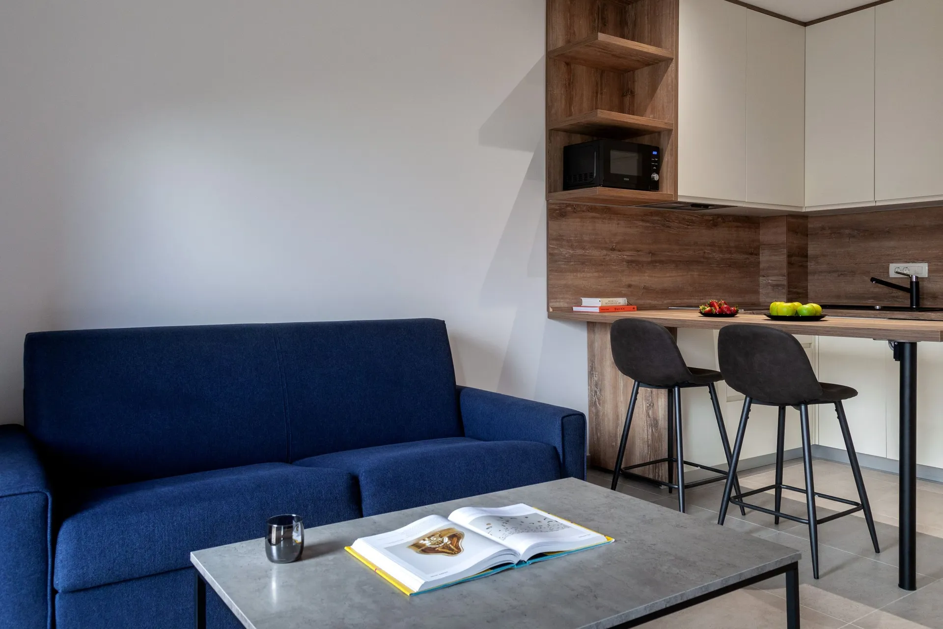 Modern living room with a blue sofa and a compact kitchen area visible in the background.