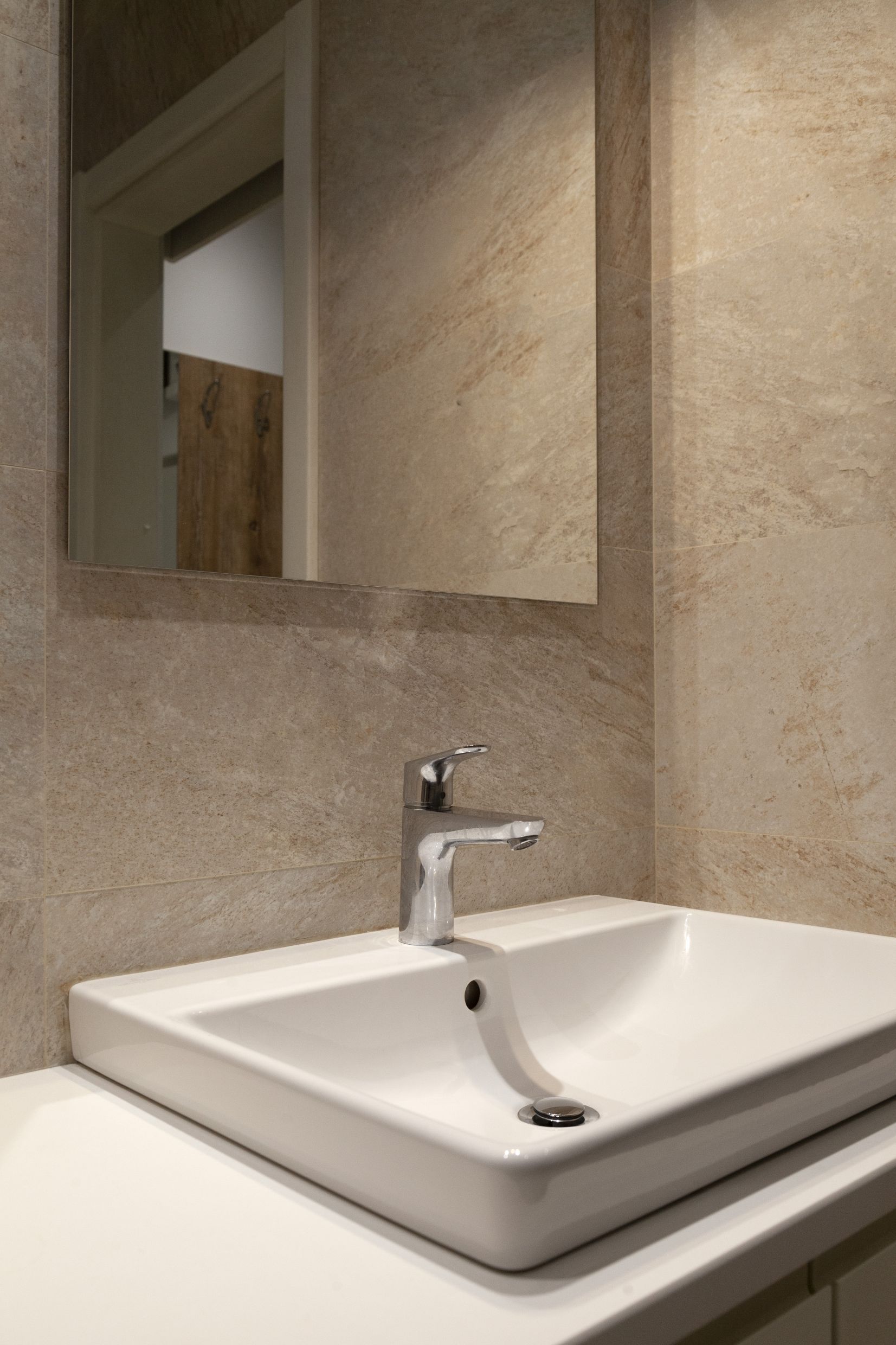 Modernes Badezimmer mit weißem Waschbecken und beigen Fliesen in einer Wohnung in Kotor, Montenegro.