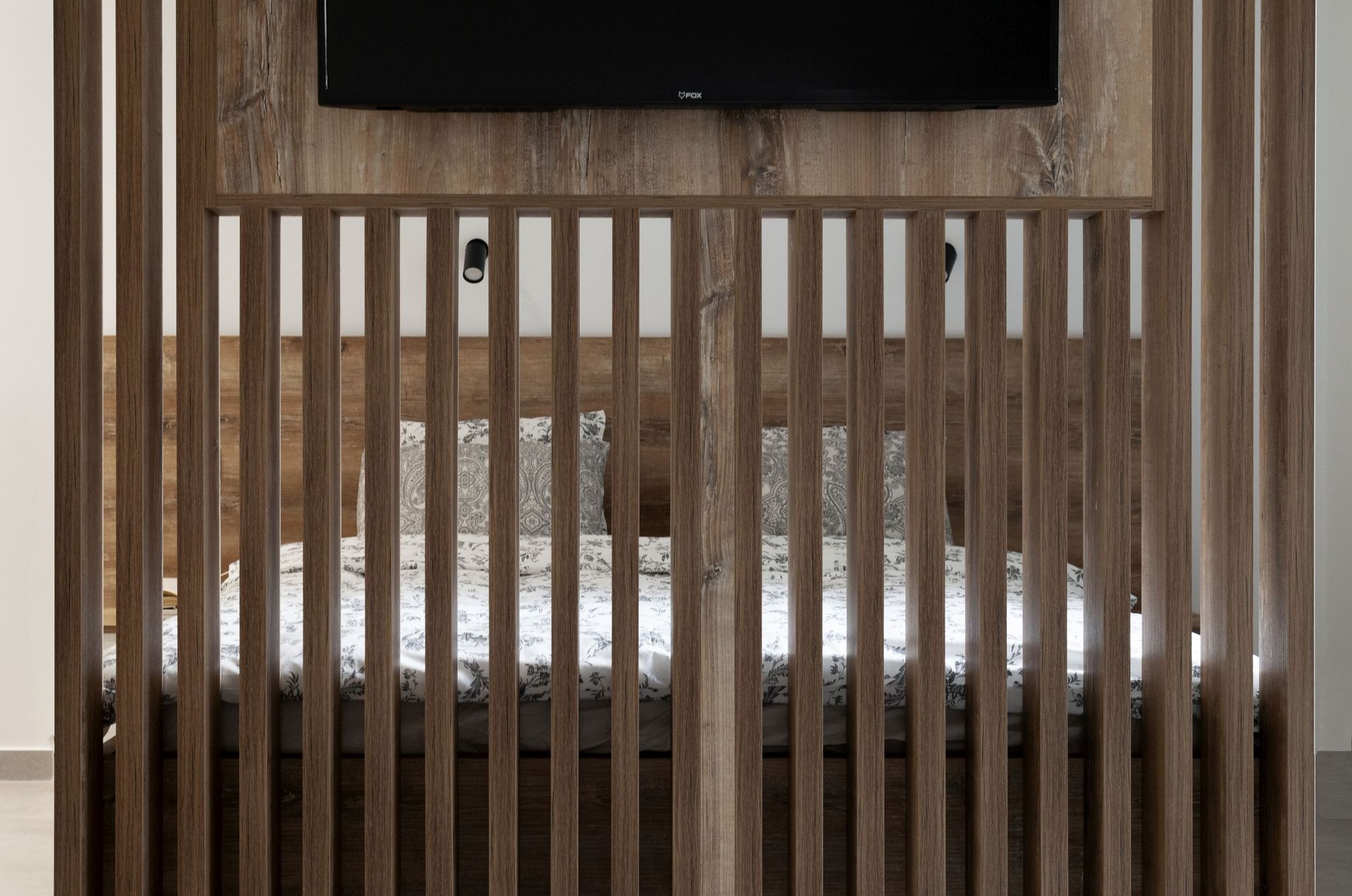Modernes Schlafzimmer in einer Wohnung in Kotor, Montenegro: Bett hinter einer dekorativen Holztrennwand mit TV-Wandpaneel.
