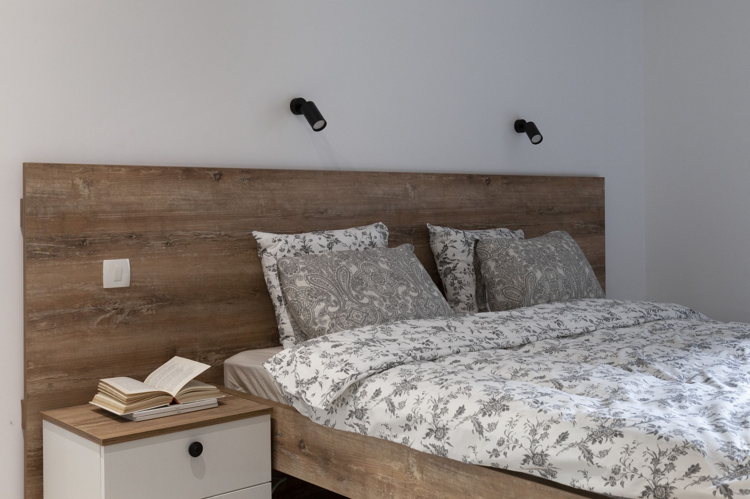 Modernes Schlafzimmer mit hölzernem Kopfteil in einer Wohnung in Kotor, Montenegro. Gemütliches Interieur mit weißen Möbeln.