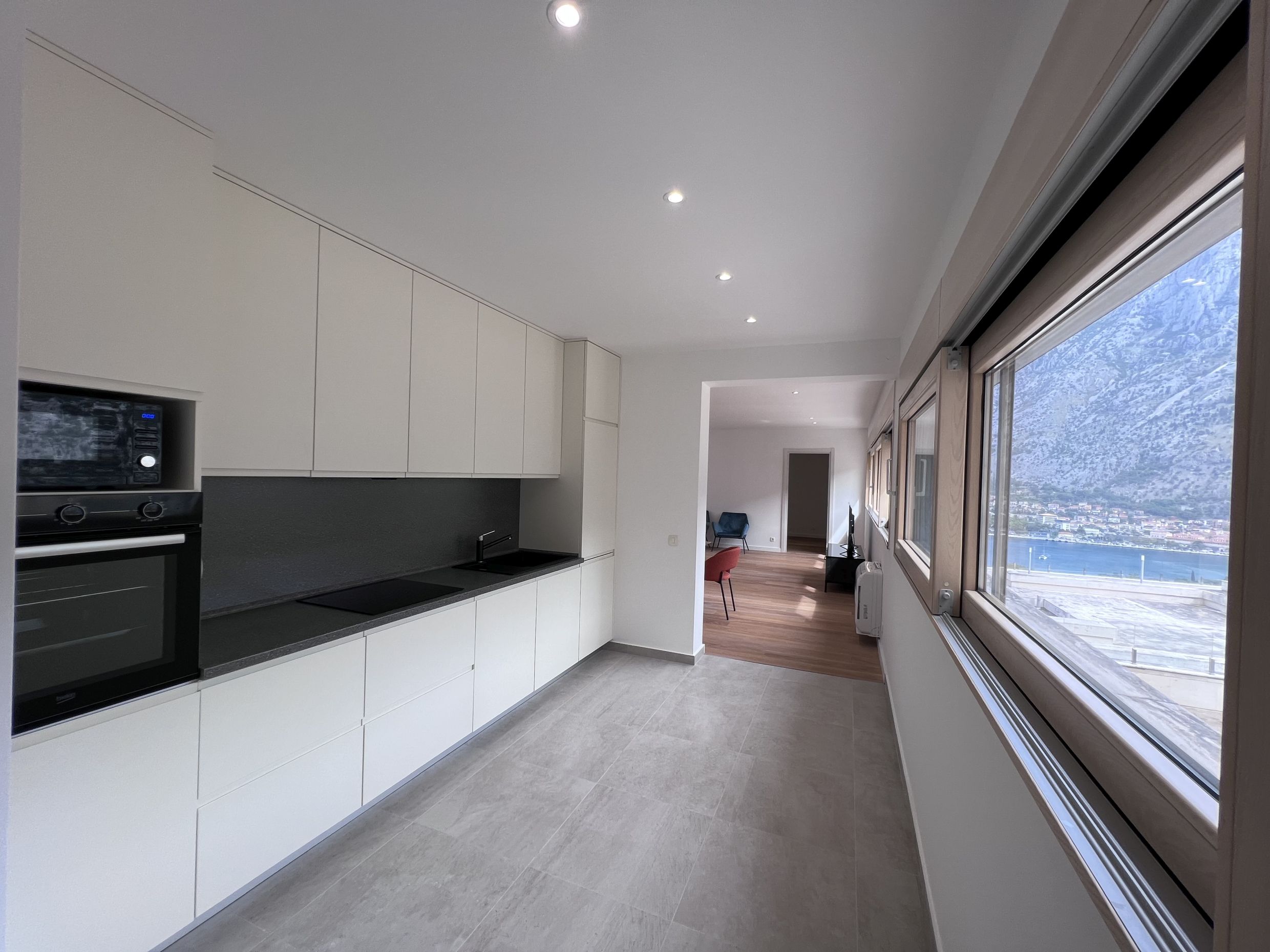Moderne Küche in einer Wohnung in Kotor, Montenegro, mit Blick auf die Bucht, weißen Fronten und Einbaugeräten.