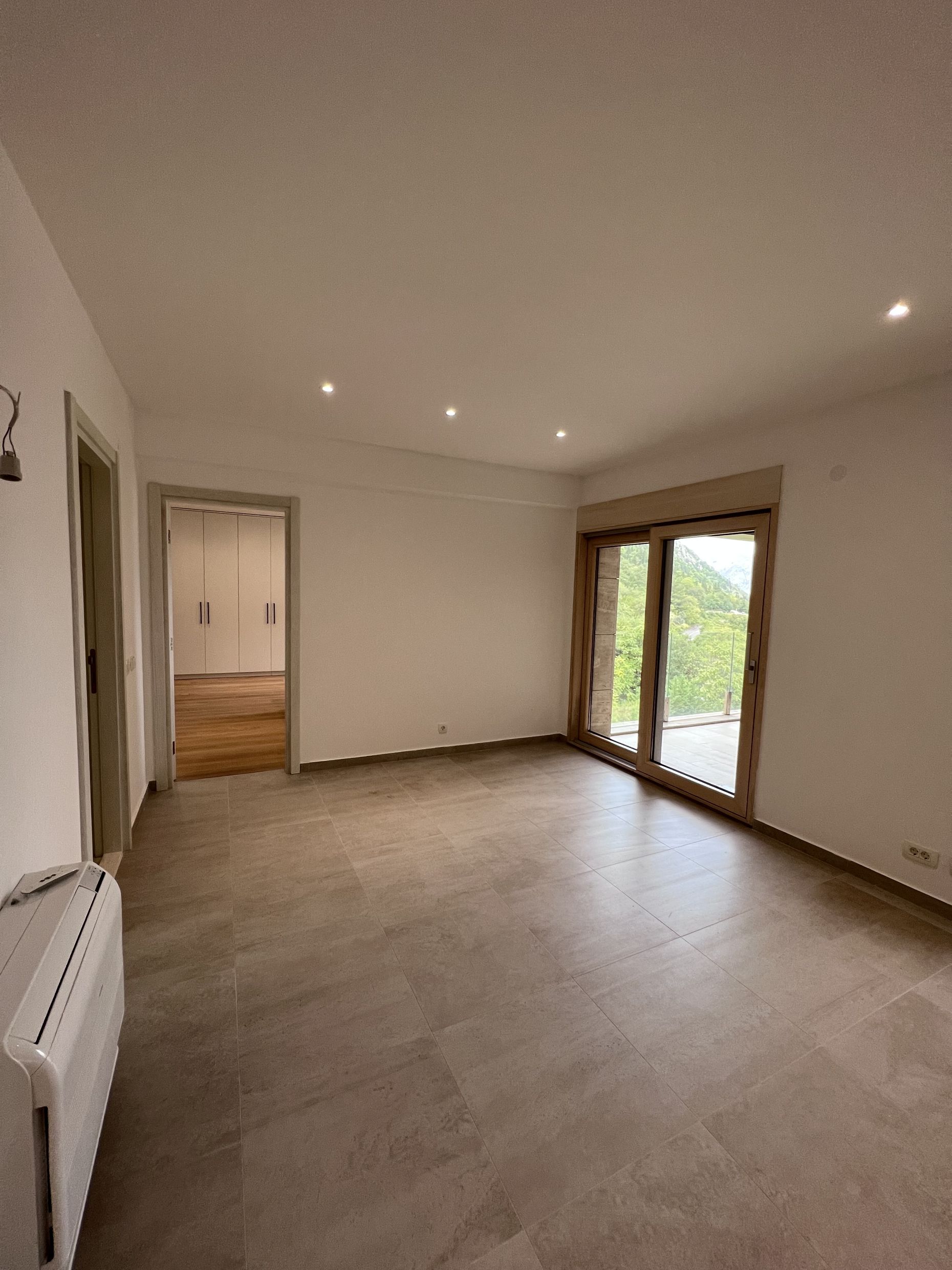Helles Wohnzimmer mit Panoramafenster und Bergblick in einer Wohnung, Kotor, Montenegro. Moderne Ausstattung und Fliesen.