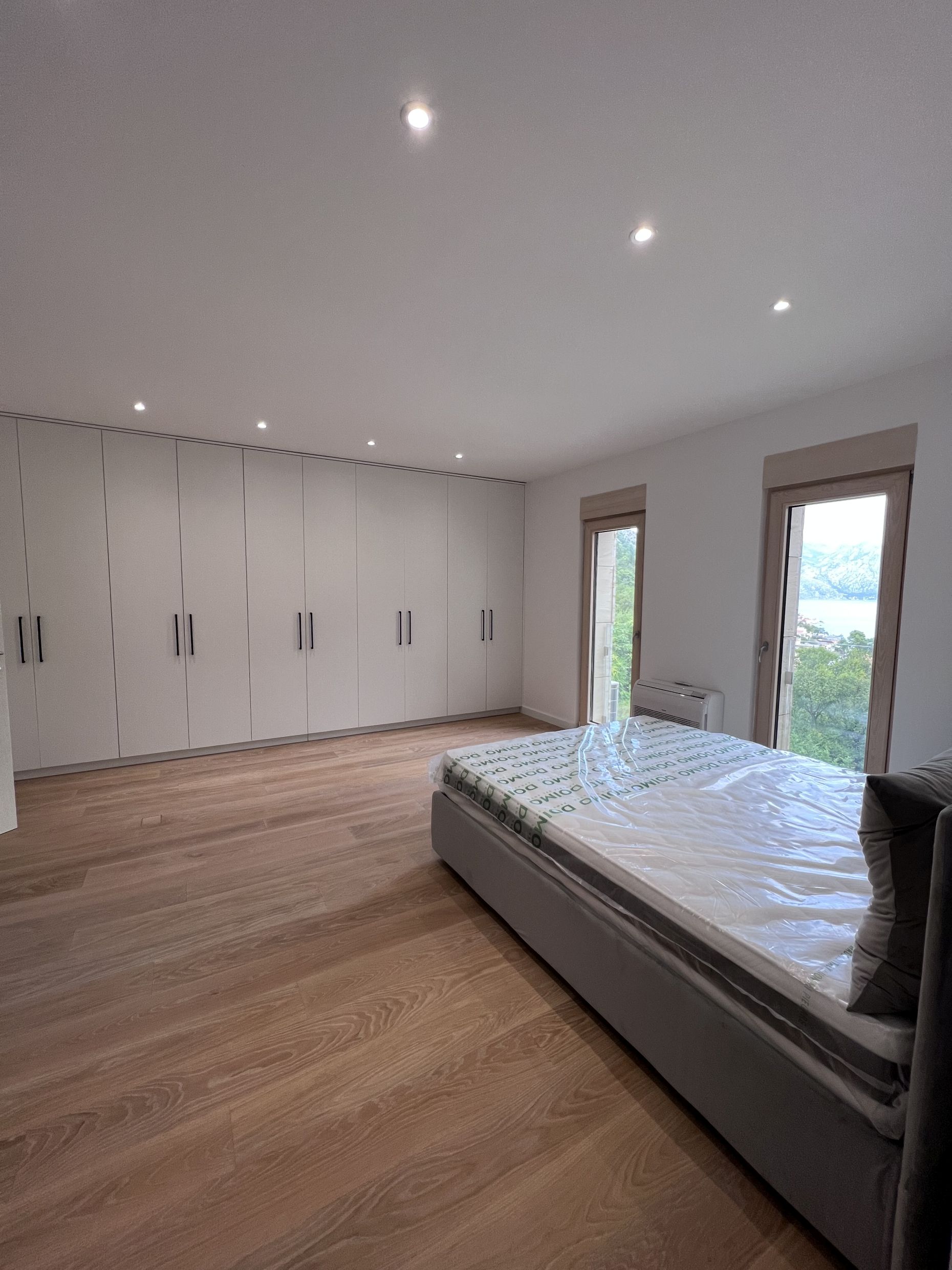 Modernes Schlafzimmer in Kotor, Montenegro: Bett, Einbauschrank über die gesamte Wand, Parkett und Meerblick aus dem Fenster.