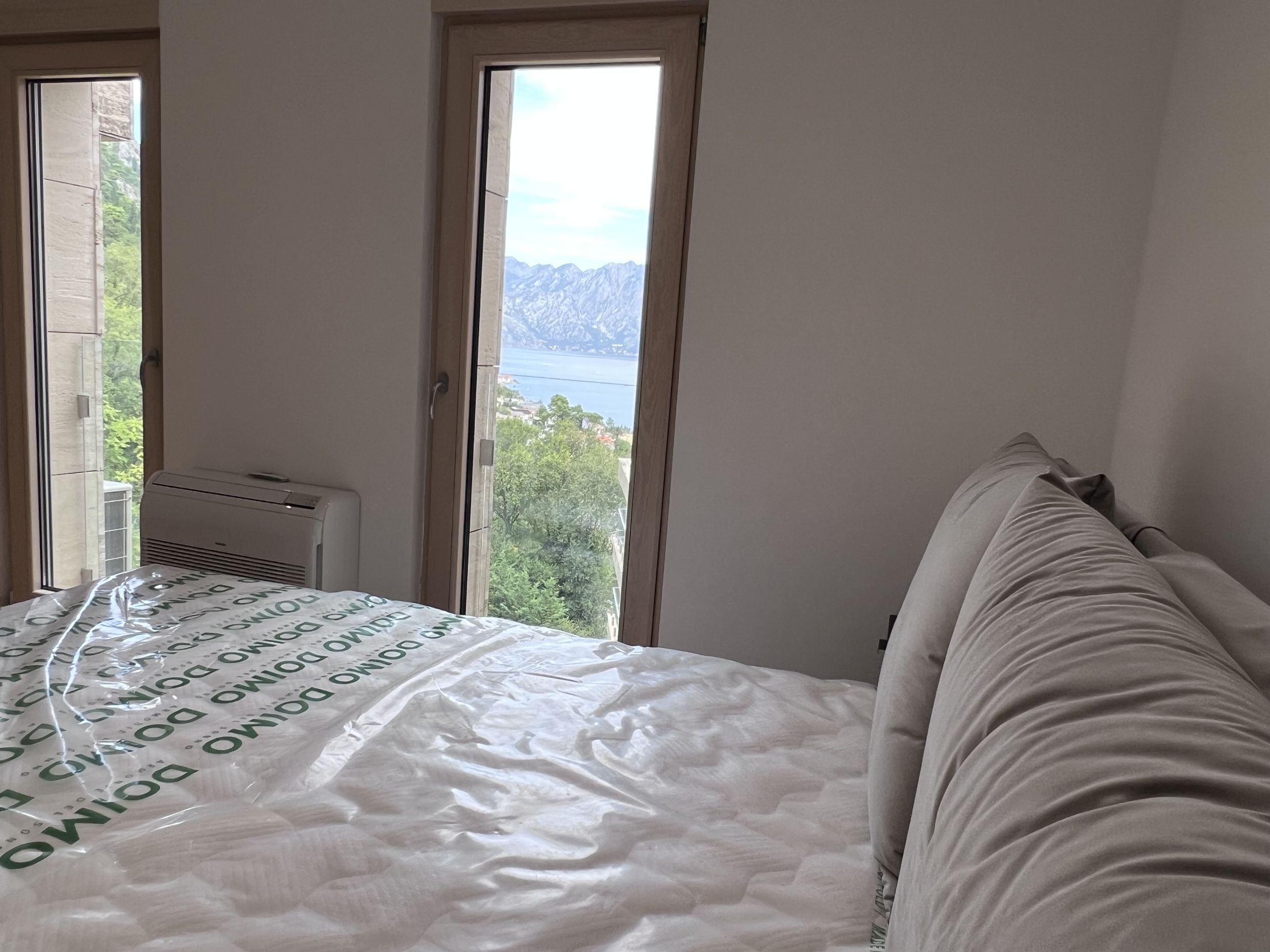Schlafzimmer in einer Wohnung in Kotor, Montenegro, mit Panoramablick auf die Bucht von Kotor und die Berge durch hohe Fenster.