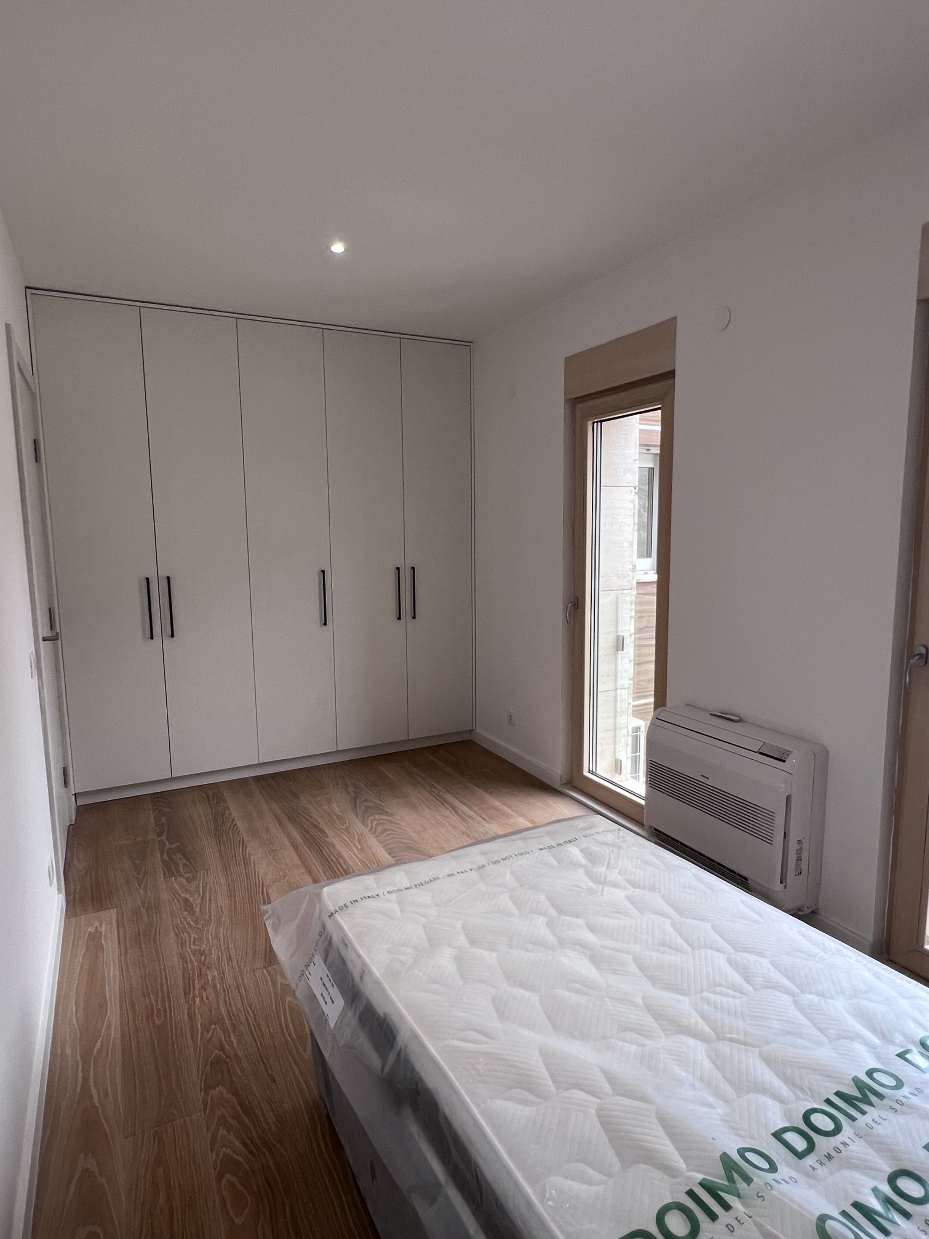 Schlafzimmer in einer Wohnung in Kotor, Montenegro: Einbauschrank, Parkettboden, Bett mit Matratze und Klimaanlage.