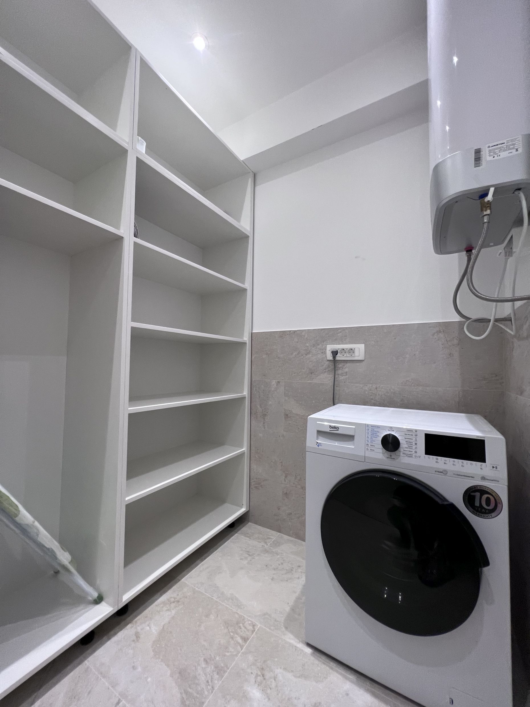 Hauswirtschaftsraum mit weißen Regalen, einer Beko-Waschmaschine und einem Boiler in der Wohnung, Kotor, Montenegro
