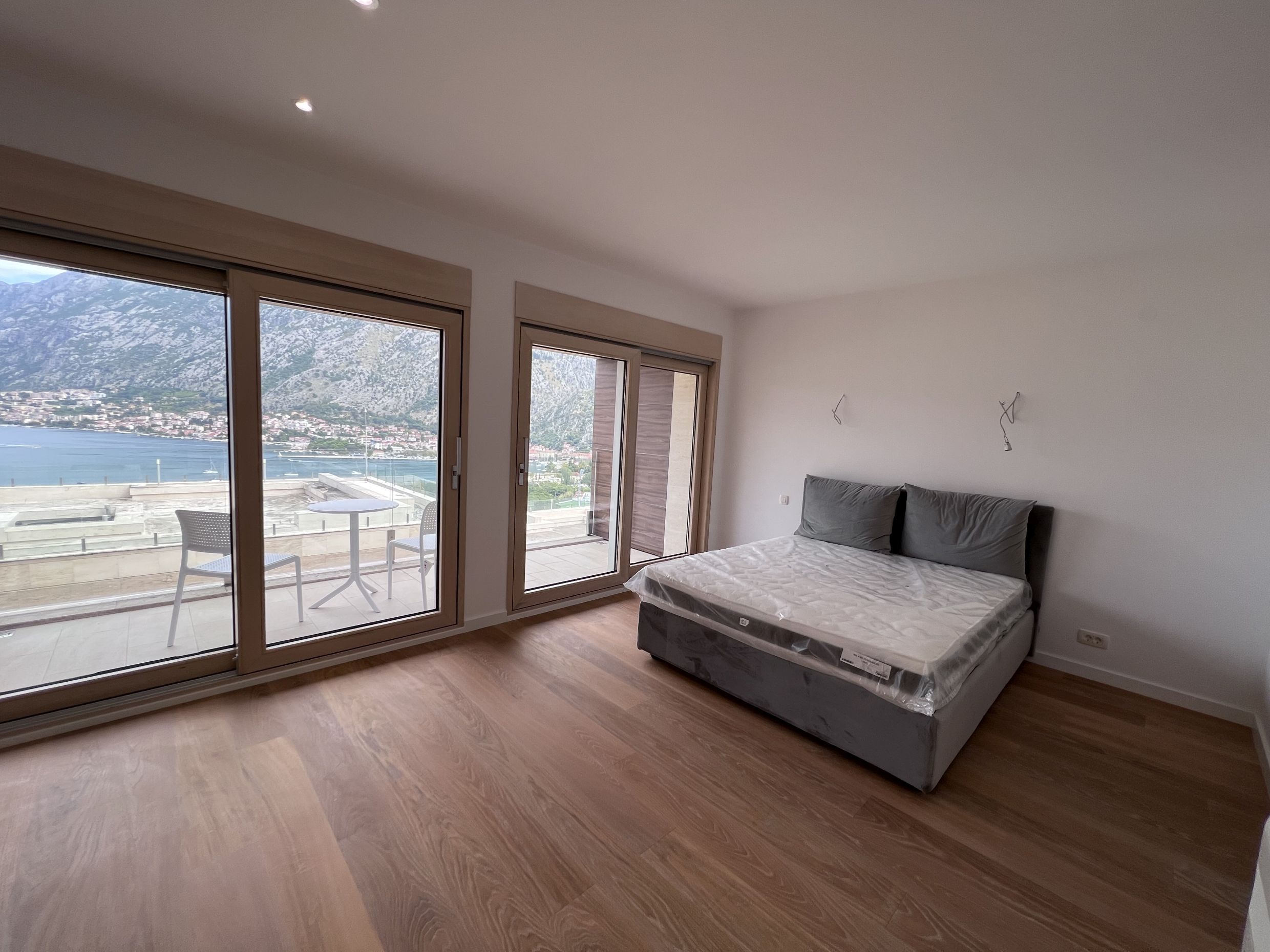 Schlafzimmer in einer Wohnung in Kotor, Montenegro: Doppelbett, Panoramafenster und Terrasse mit Blick auf die Bucht von Kotor.