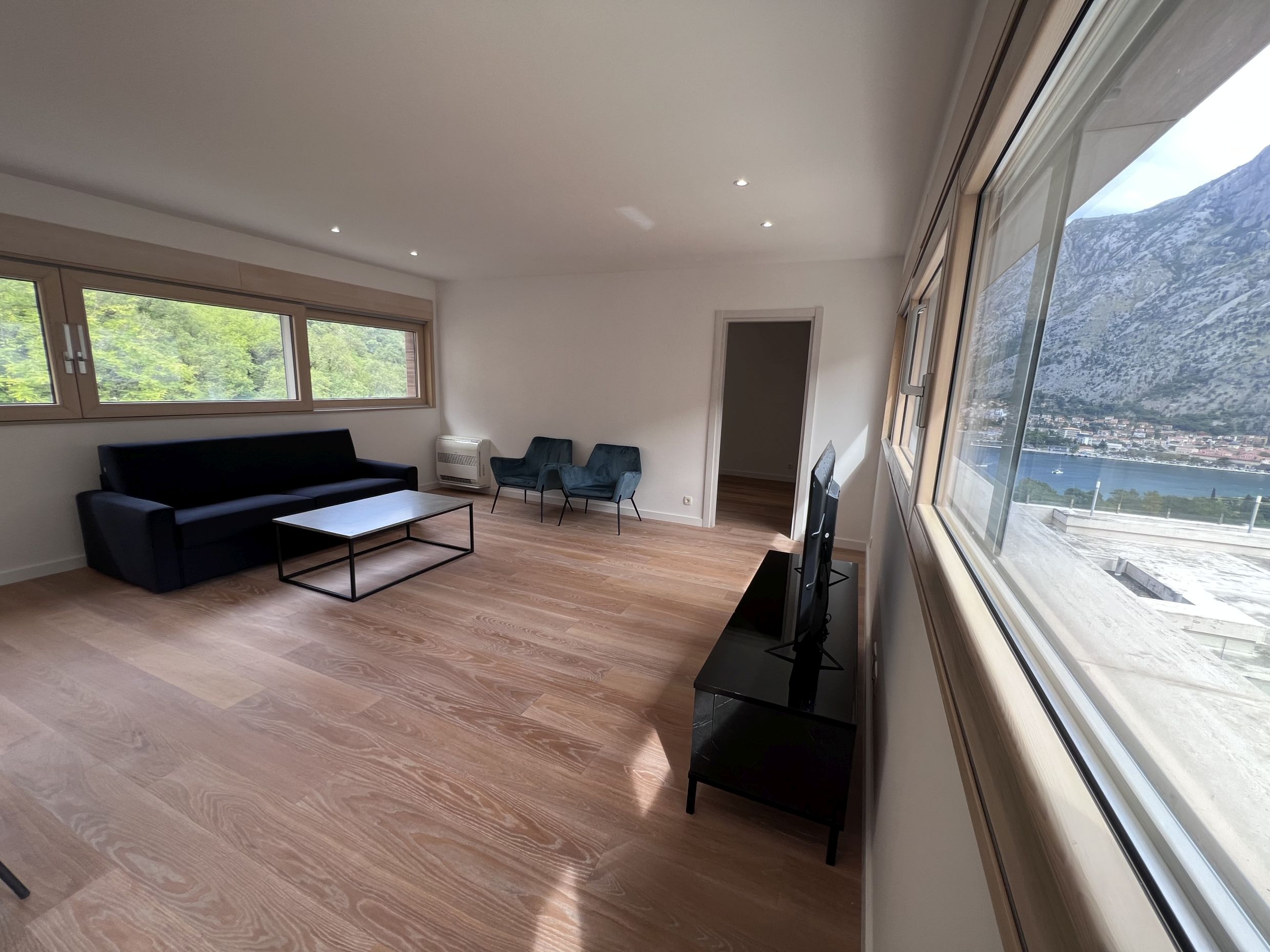 Wohnzimmer in einer Wohnung in Kotor, Montenegro: moderne Möbel, Panoramafenster mit Blick auf die Bucht von Kotor und die Berge.