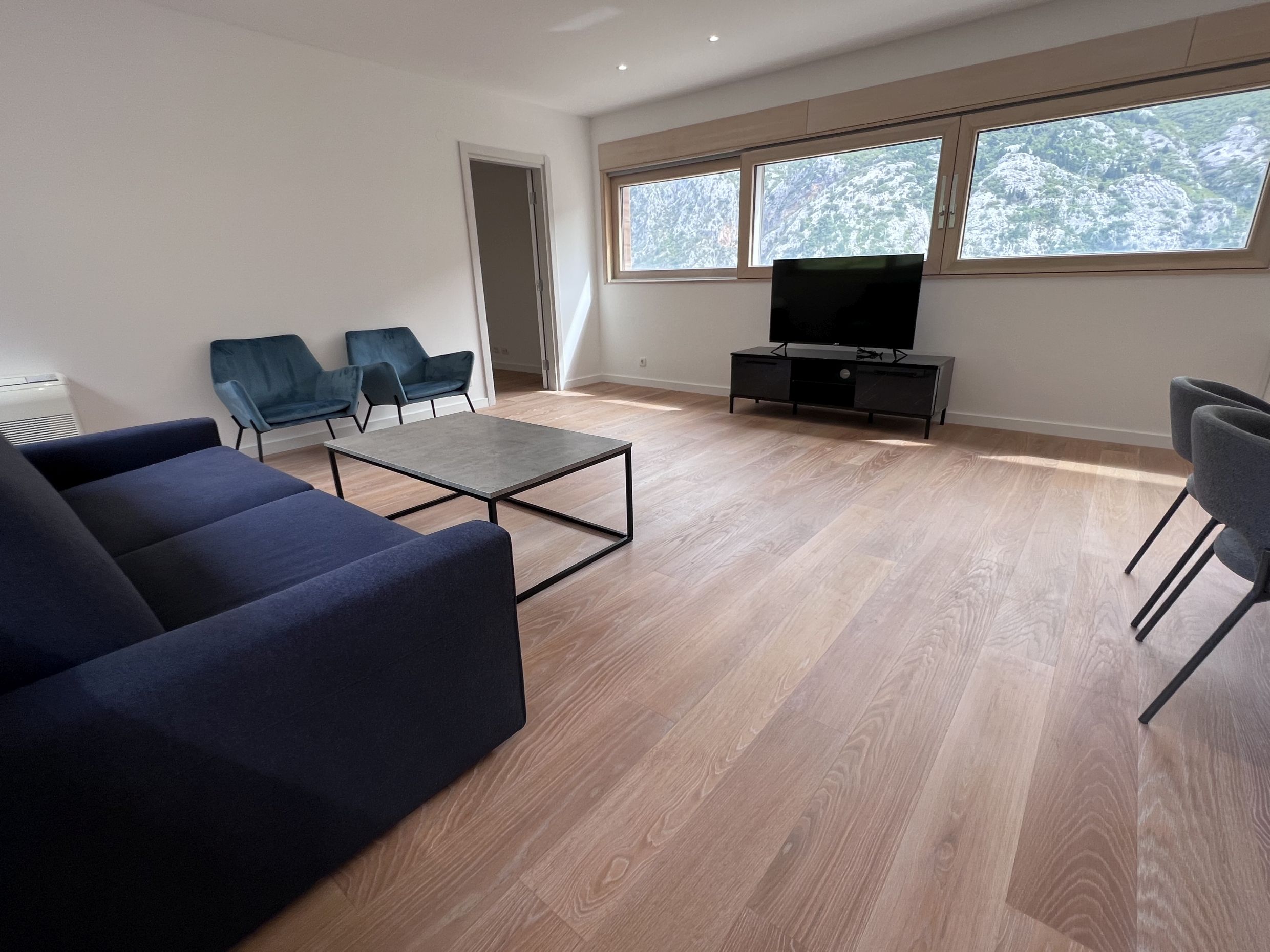 Modernes Wohnzimmer in einer Wohnung in Kotor, Montenegro: blaues Sofa, Panoramafenster mit Bergblick, helles Interieur.