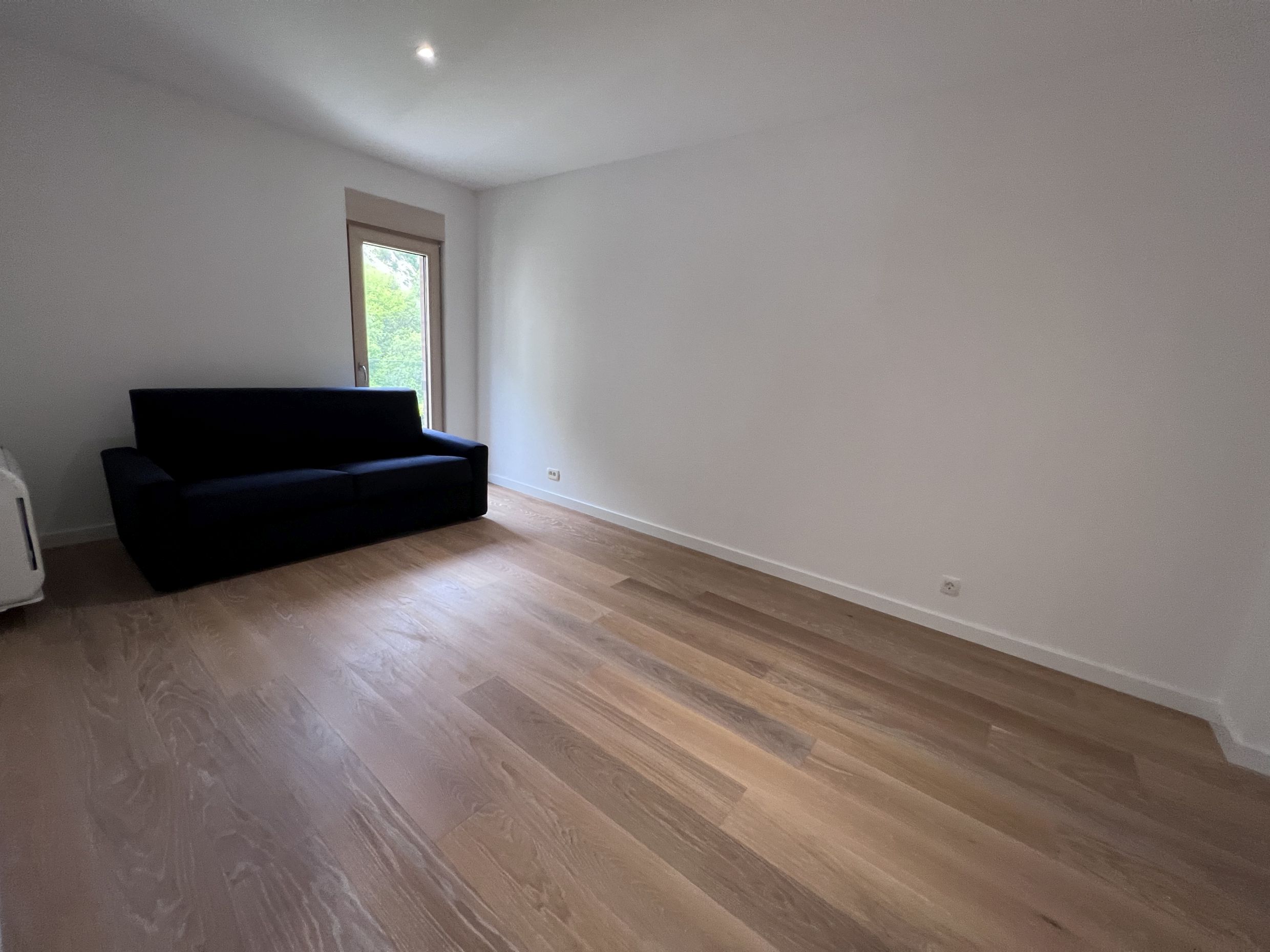 Helles Wohnzimmer mit Parkett und dunklem Sofa in einer Wohnung in Kotor, Montenegro. Modernes Interieur mit weißen Wänden.