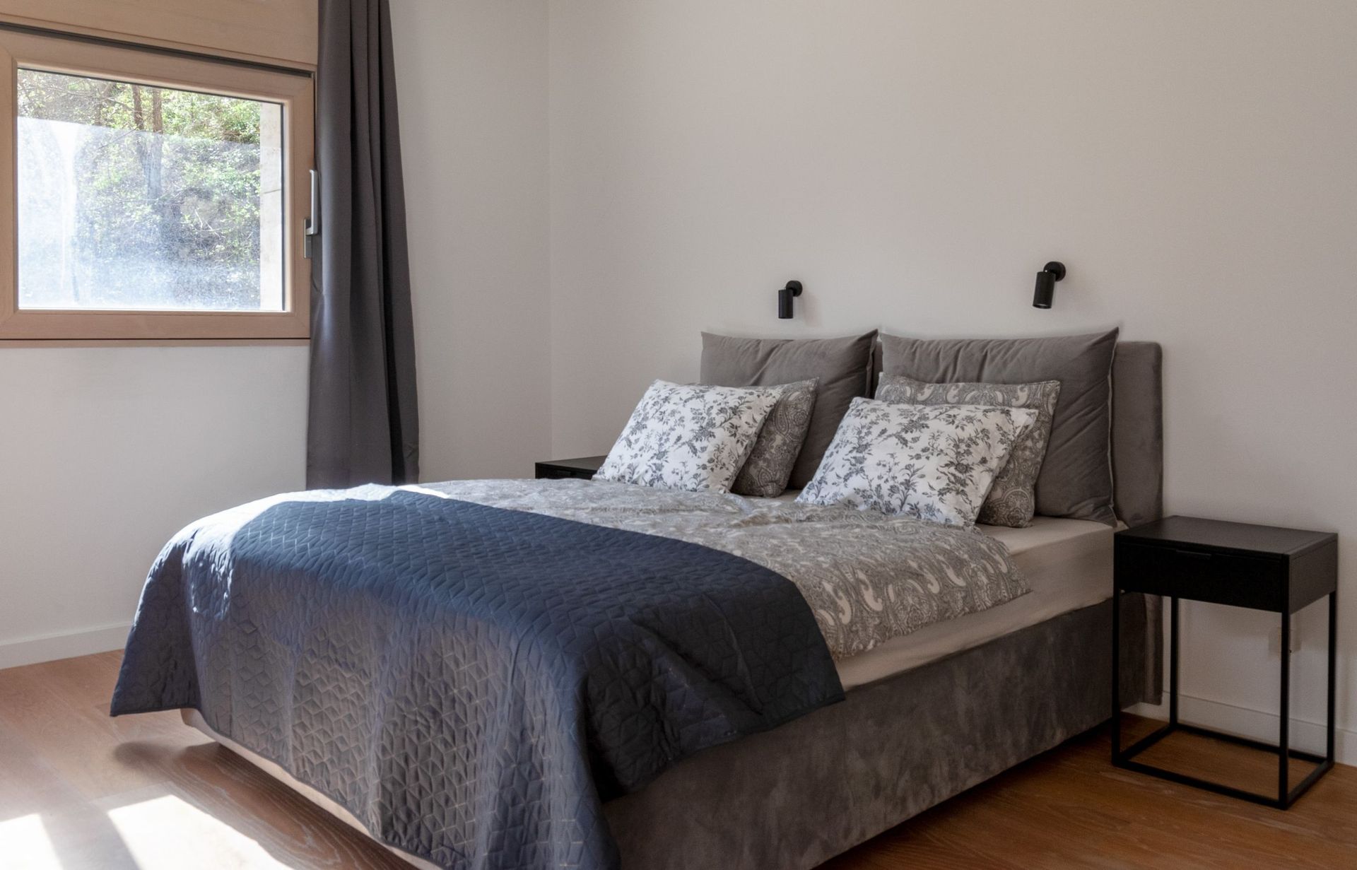 Gemütliches Schlafzimmer mit Doppelbett in einer Wohnung in Kotor, Montenegro: moderne Möbel und Blick ins Grüne aus dem Fenster.