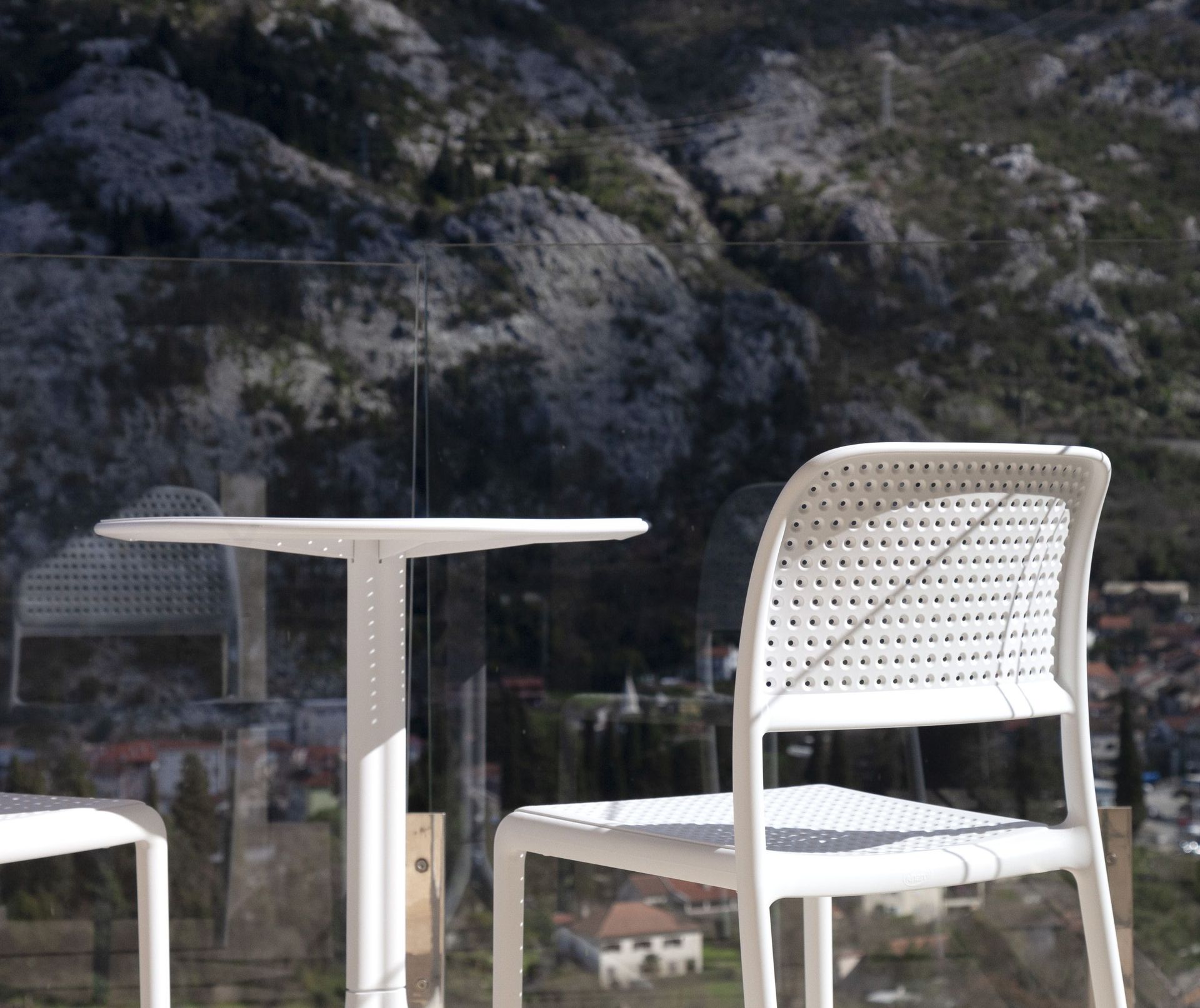 Weiße Stühle und ein Tisch auf dem Balkon der Wohnung in Kotor, Montenegro, mit Panoramablick auf die Berge und die Stadt.