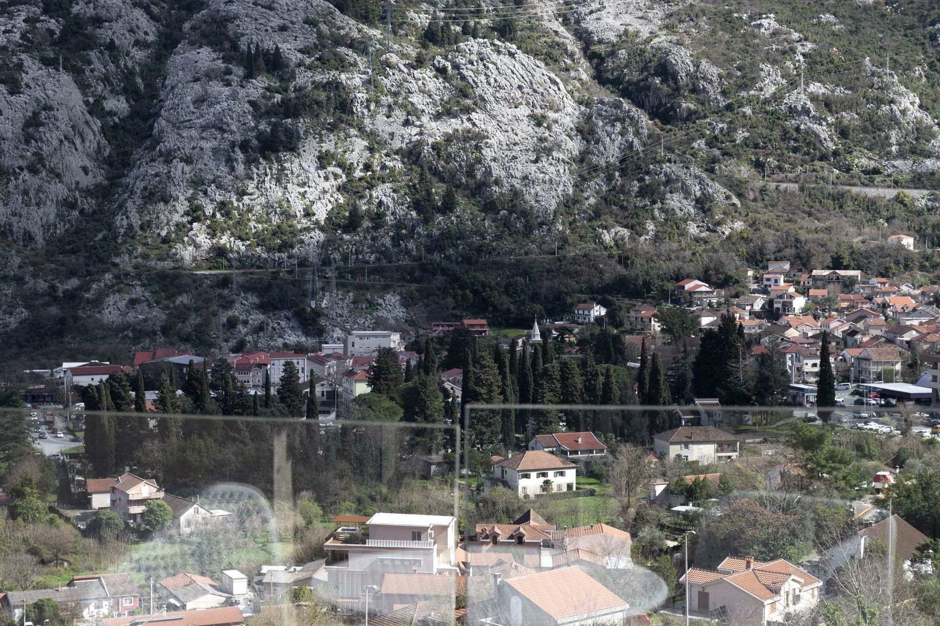 Panoramablick aus dem Fenster der Wohnung auf die Berge und die Stadt Kotor in Montenegro von der Terrasse mit Glasgeländer.