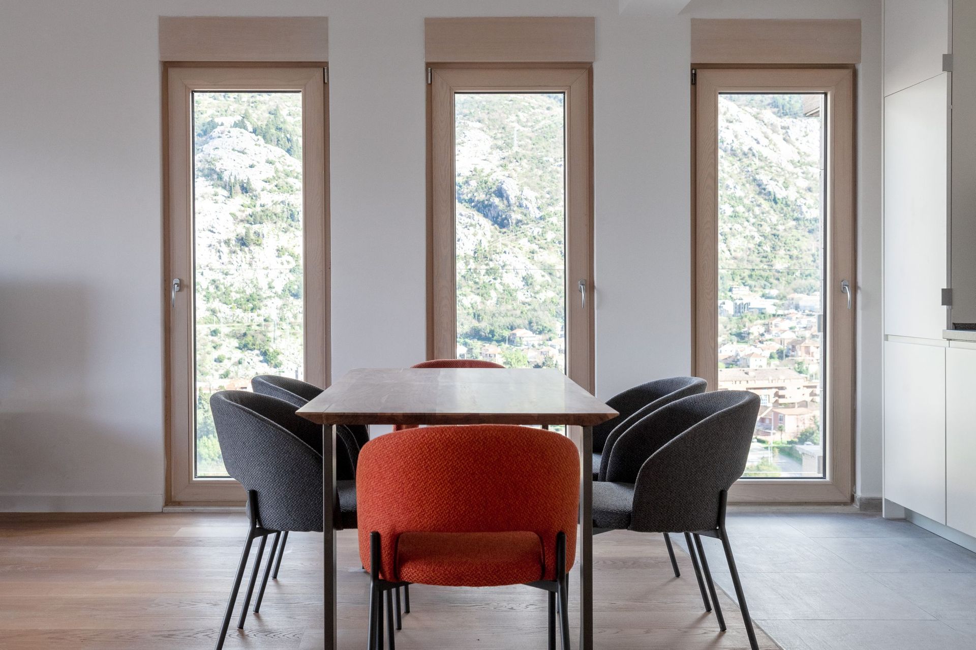Essbereich in einer modernen Wohnung in Kotor, Montenegro: Holztisch, graue und orange Stühle, Blick auf die Berge.