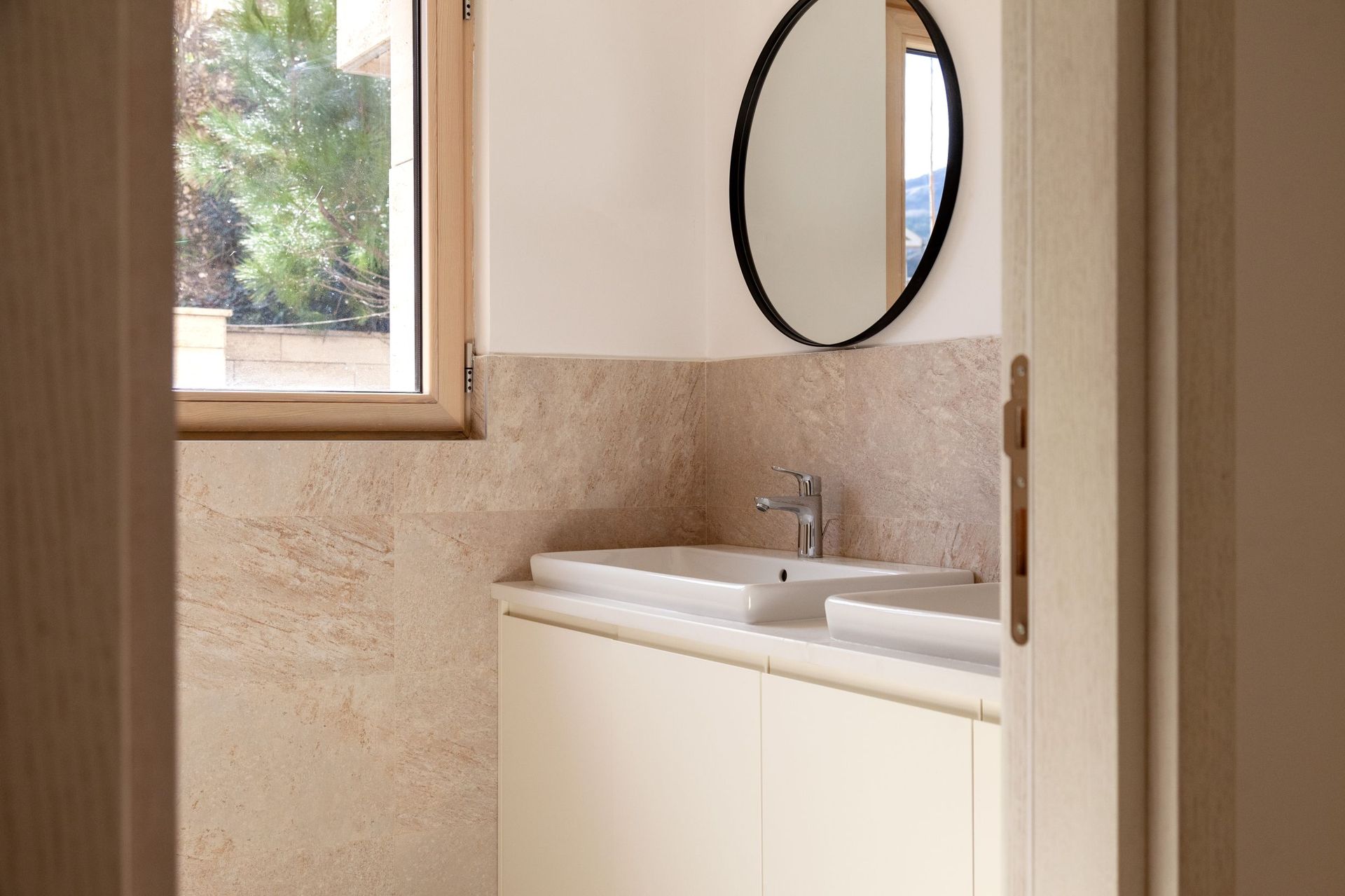 Modernes Badezimmer mit Doppelwaschbecken in einer Wohnung in Kotor, Montenegro: beige Fliesen und runder Spiegel.