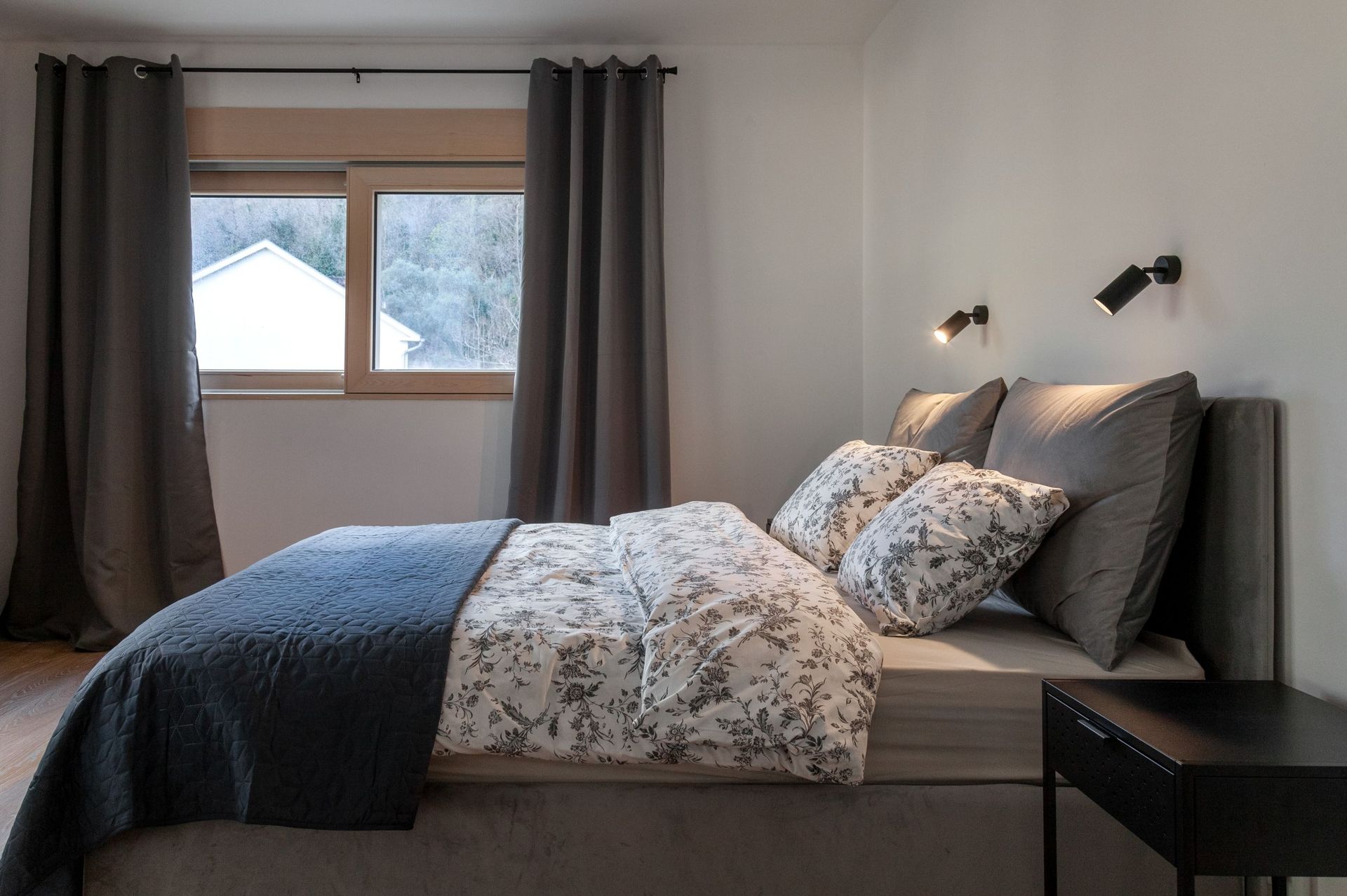 Modernes Schlafzimmer in einer Wohnung in Kotor, Montenegro: Doppelbett, graue Textilien und Bergblick aus dem Fenster.