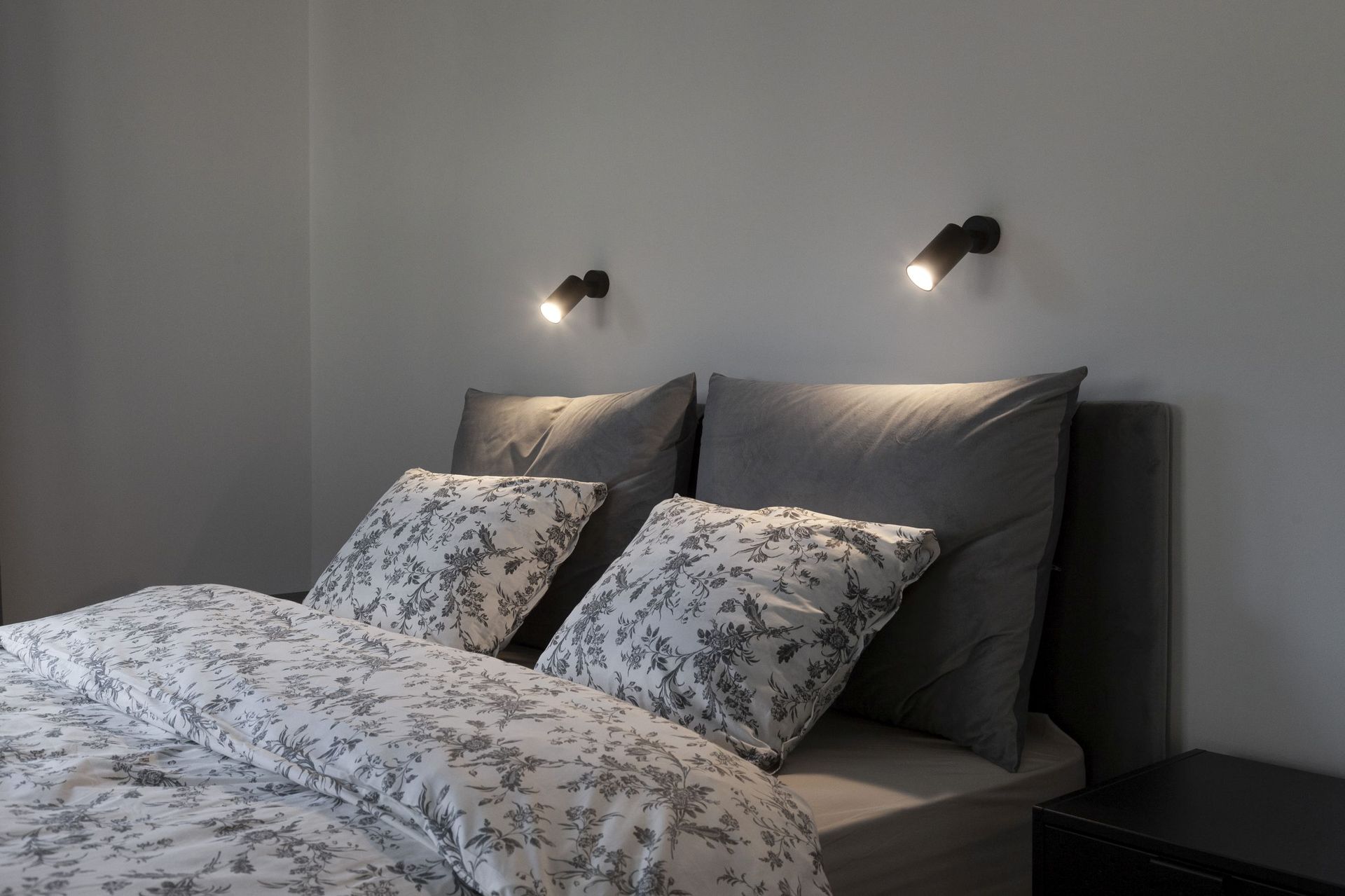 Modernes Schlafzimmer in einer Wohnung in Kotor, Montenegro: Doppelbett mit grauer Bettwäsche und Wandleuchten.