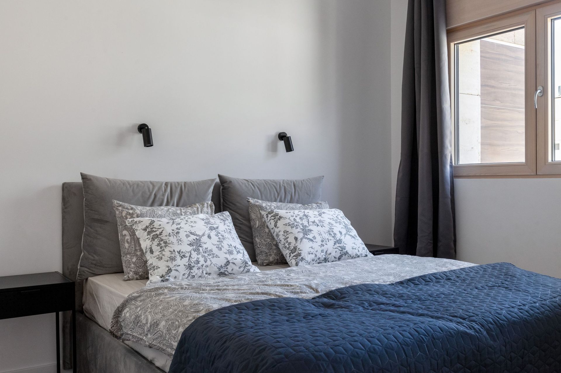 Modernes Schlafzimmer mit Doppelbett in einer Wohnung in Kotor, Montenegro: graue Textilien und stilvolle Wandleuchten.