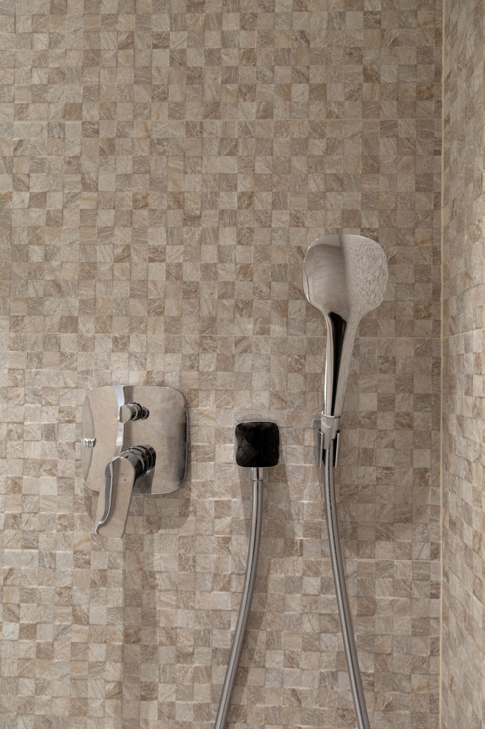 Moderne Duschbrause und Armatur vor beiger Mosaikfliese im Badezimmer einer Wohnung in Kotor, Montenegro.