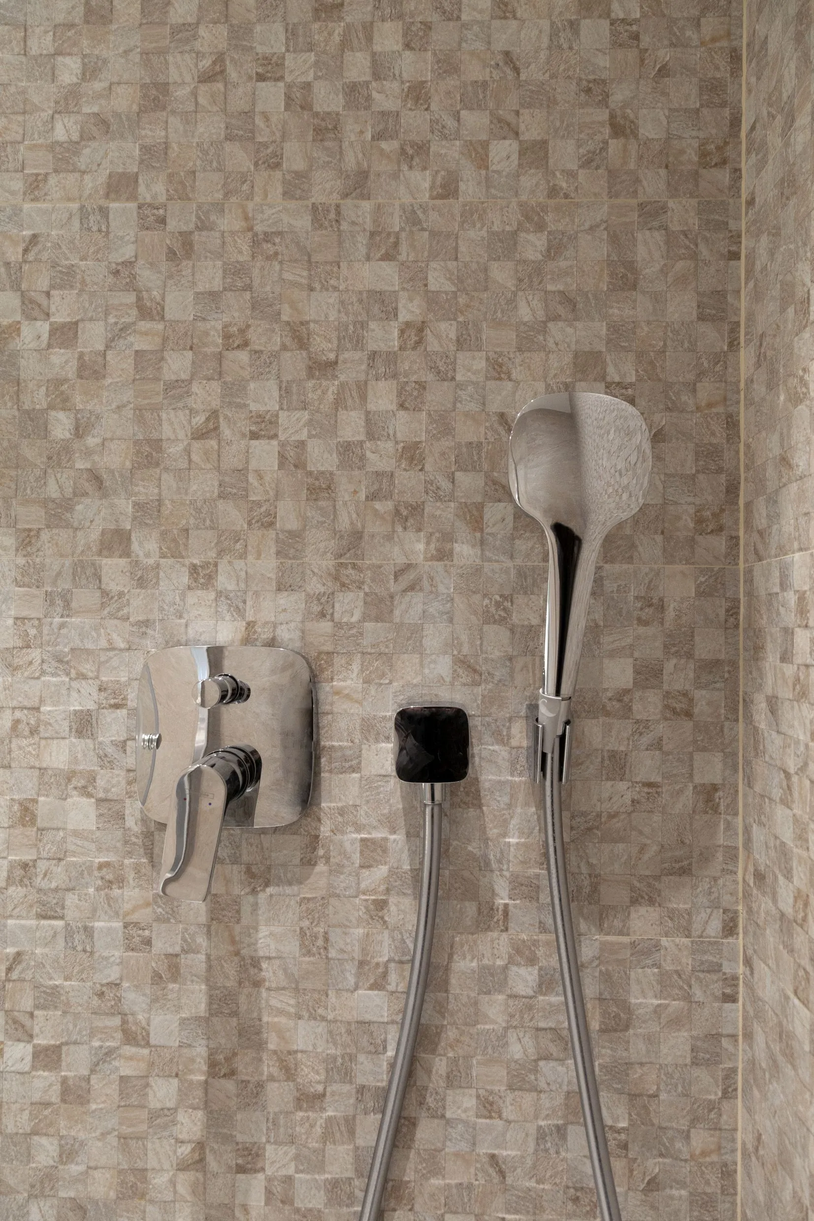 Shower area with beige mosaic tile, chrome mixer valve, and handheld showerhead mounted on the wall.