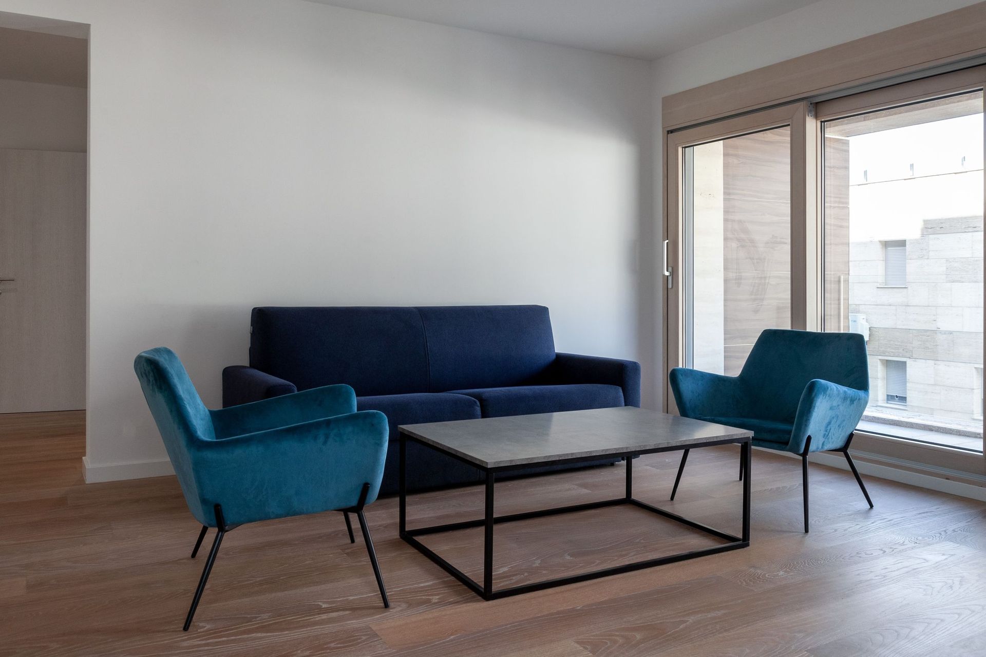 Modernes Wohnzimmer mit blauem Sofa und Sesseln in einer Wohnung in Kotor, Montenegro, mit Panoramafenster und Parkett.
