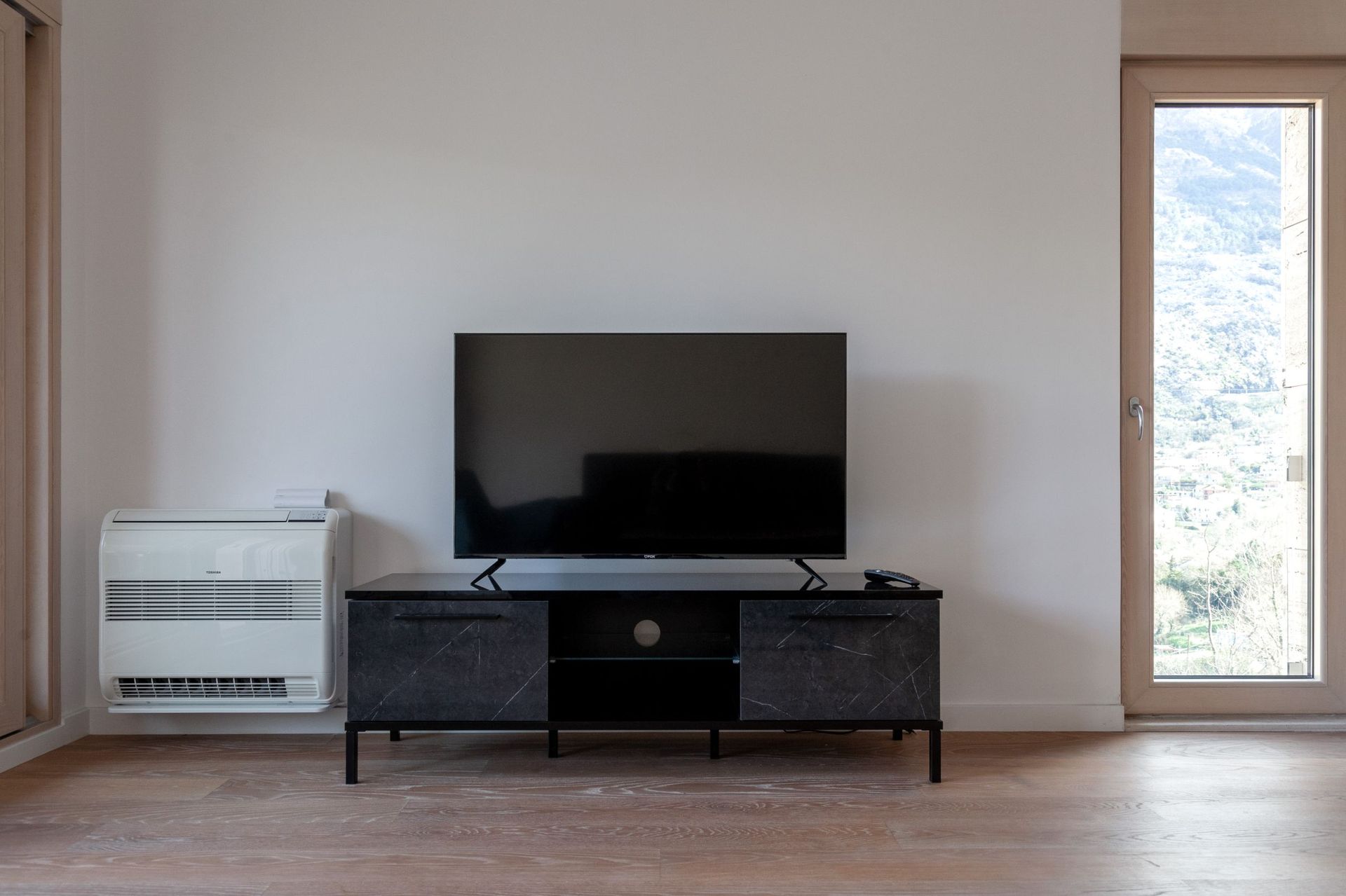 Wohnzimmer in einer Wohnung in Kotor, Montenegro: TV-Bereich mit marmorierter TV-Kommode, Klimaanlage und Bergblick aus dem Fenster.