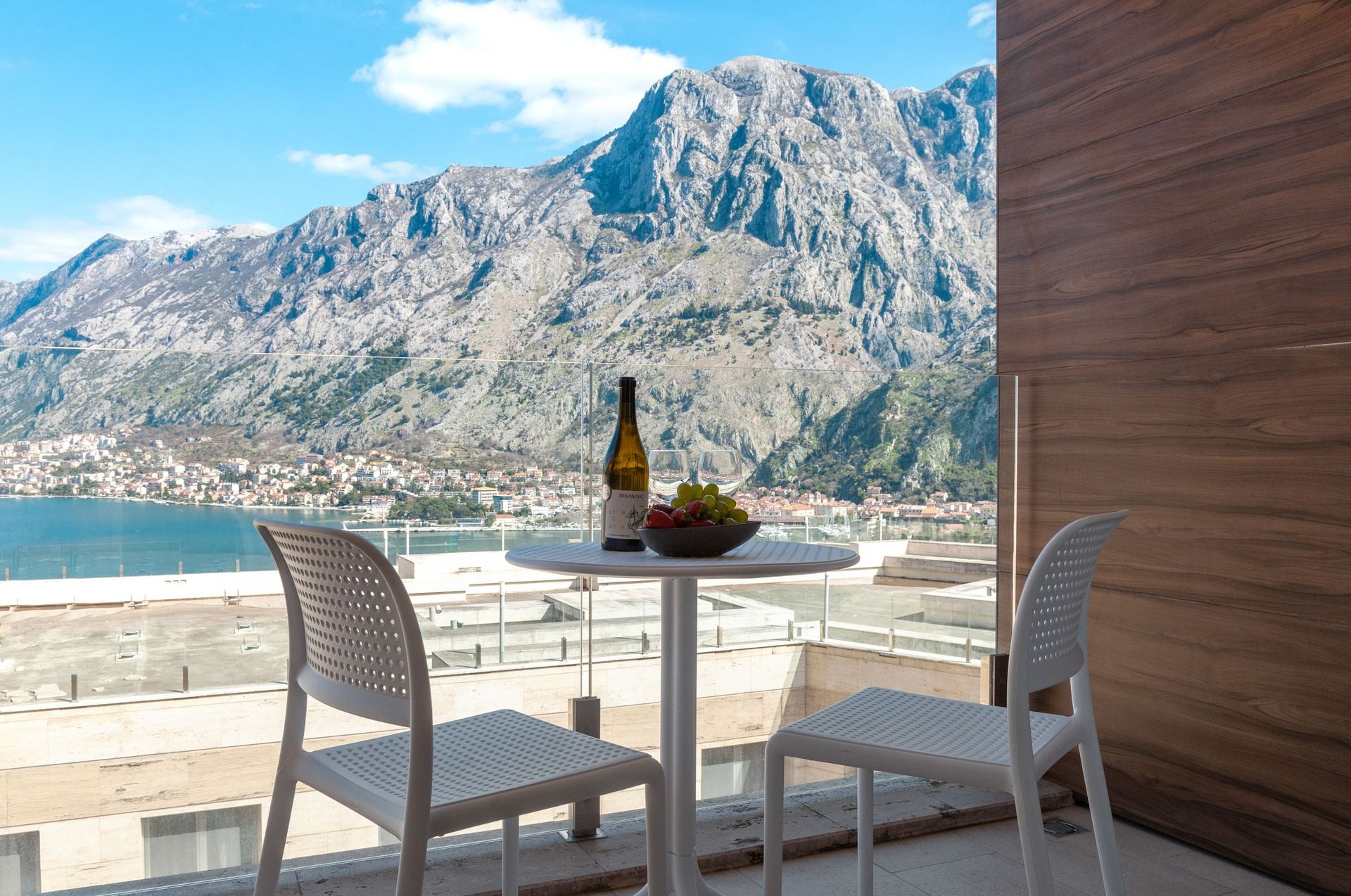 Balkon mit Blick auf die Bucht von Kotor und die Berge in einer Wohnung, Kotor, Montenegro: Tisch mit Wein und Früchten, modernes Design.