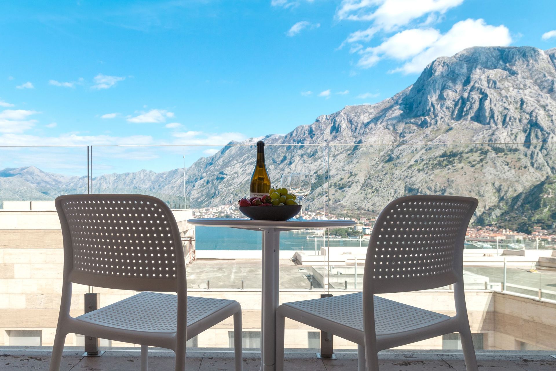Balkon mit Blick auf die Bucht von Kotor und die Berge in einer Wohnung, Montenegro: Tisch mit Wein und Früchten, moderne Möbel.
