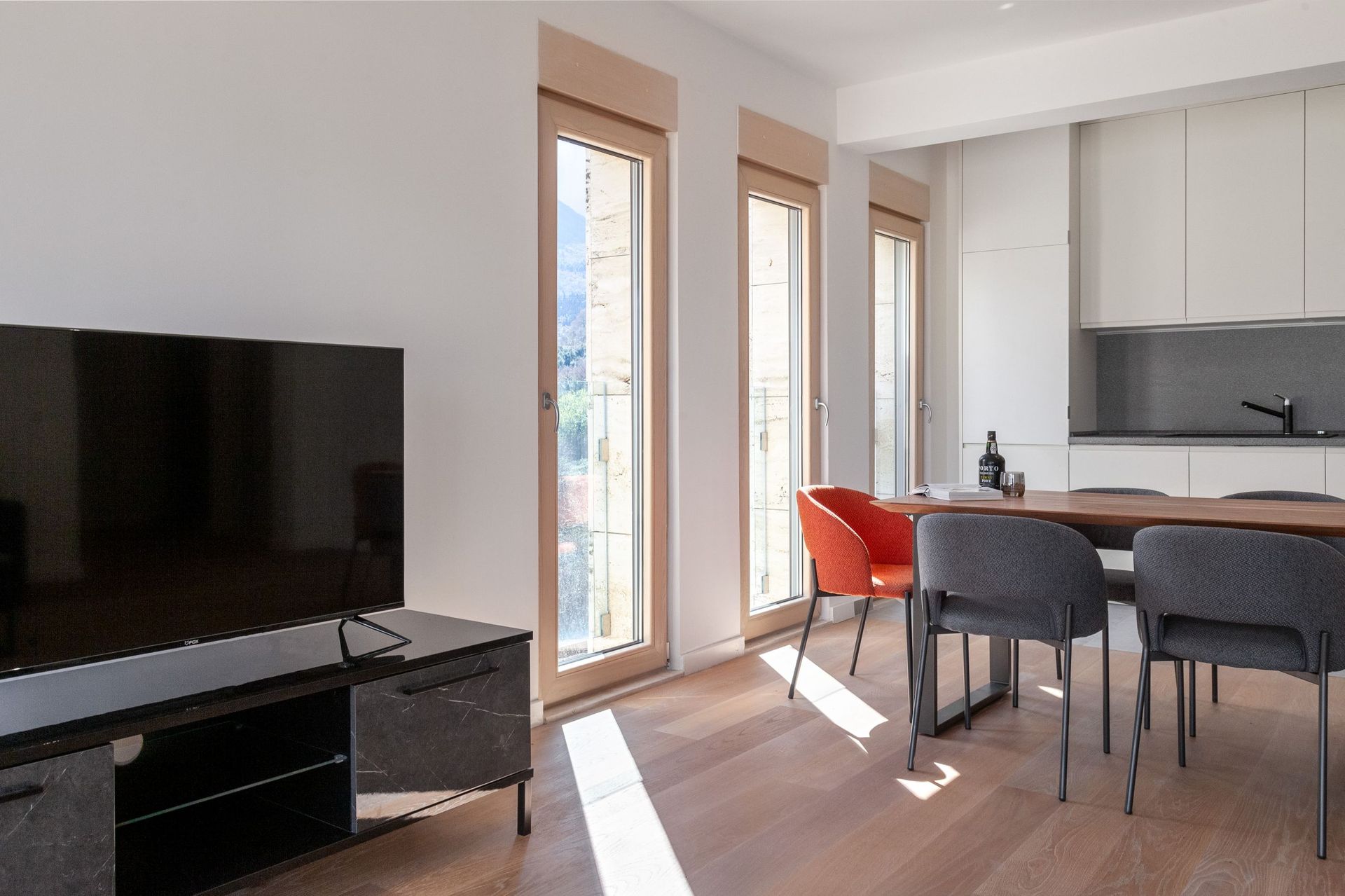 Modernes Wohnzimmer mit Küche in einer Wohnung in Kotor, Montenegro: Essbereich, Panoramafenster und helles Interieur.