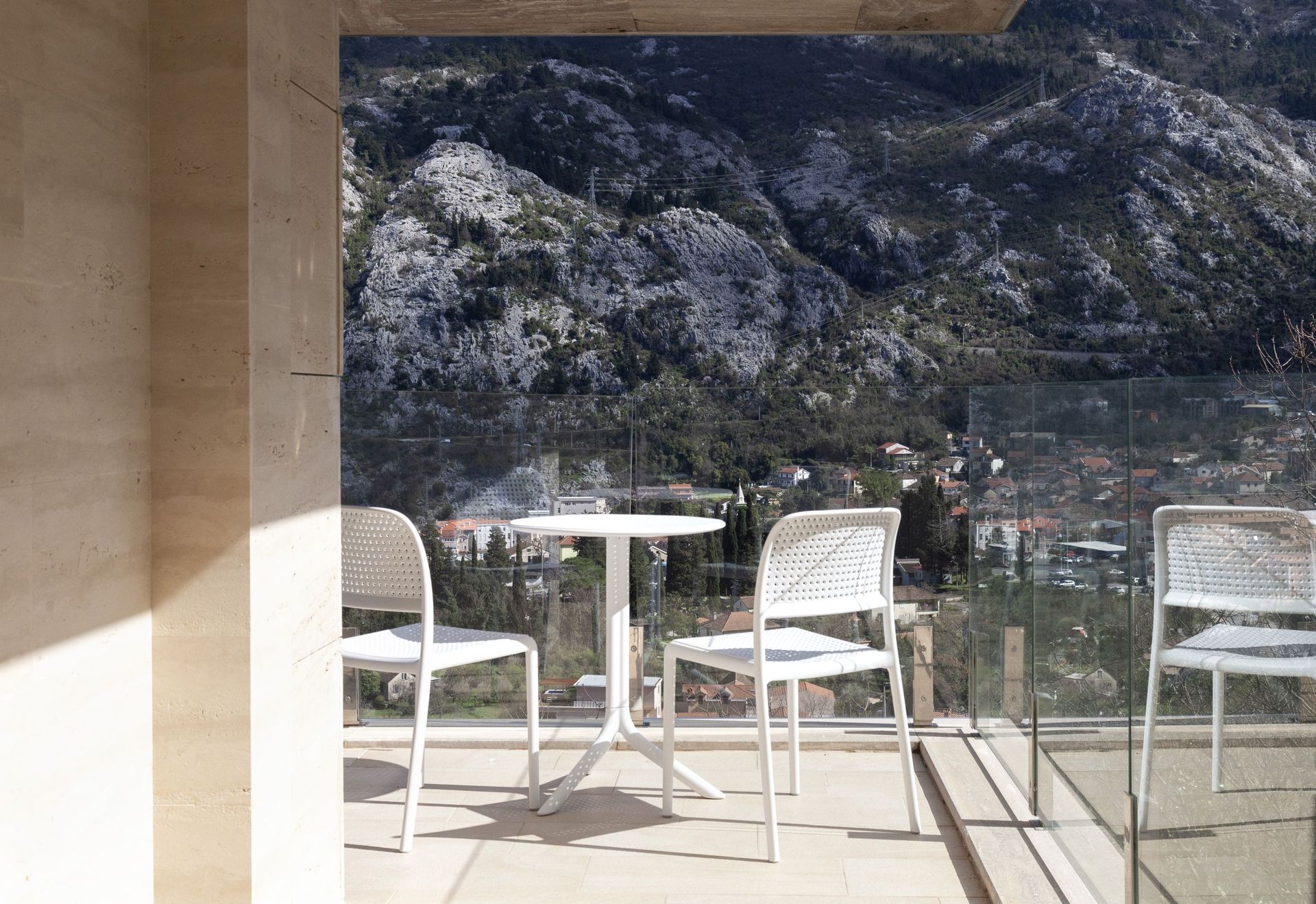 Balkon mit weißen Möbeln und Panoramablick auf die Berge und die Stadt Kotor, Montenegro. Moderne Ausstattung und Glasgeländer.