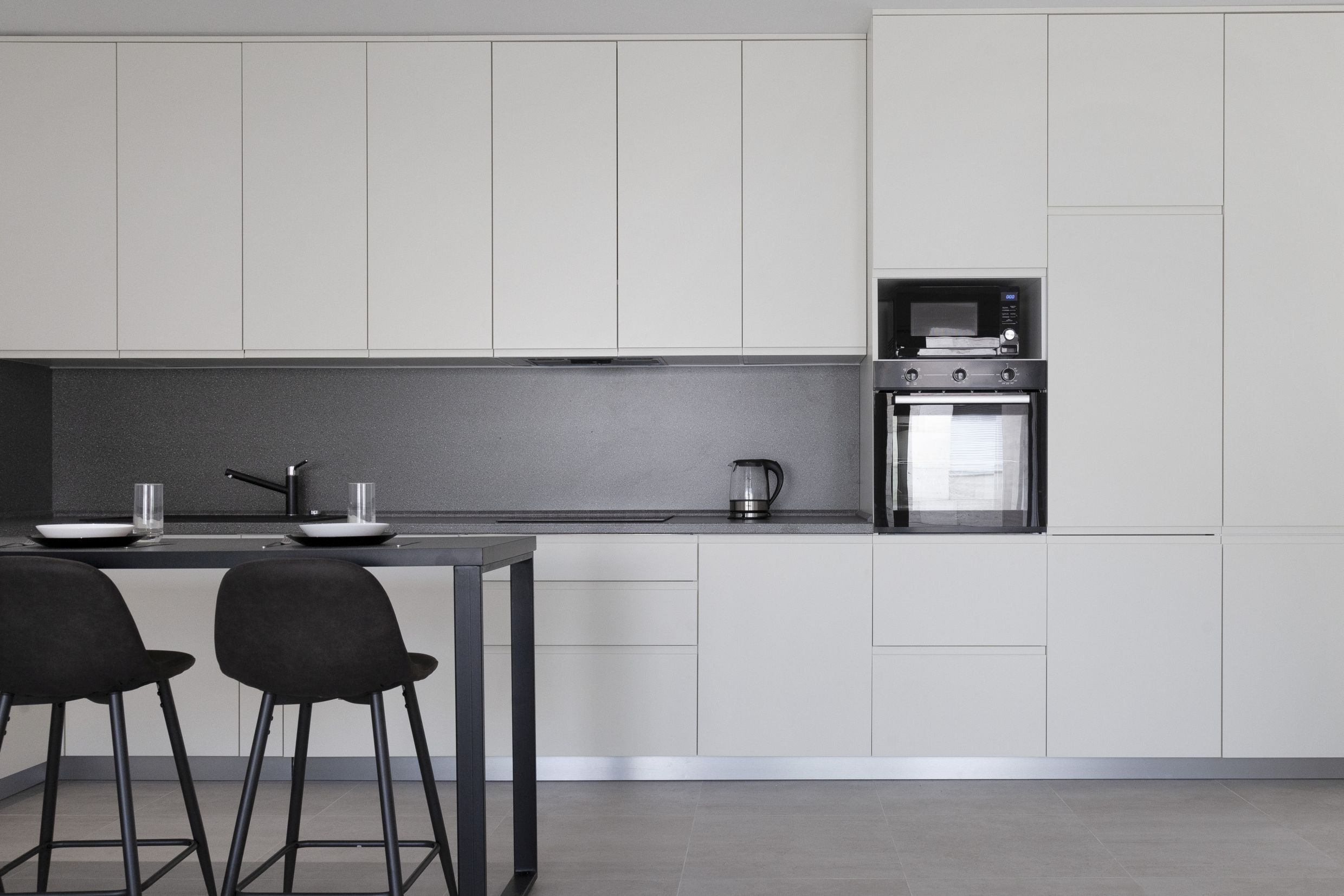 Moderne Küche in einer Wohnung in Kotor, Montenegro: helle Einbauküche, integrierte Geräte und eine Bartheke mit Stühlen.