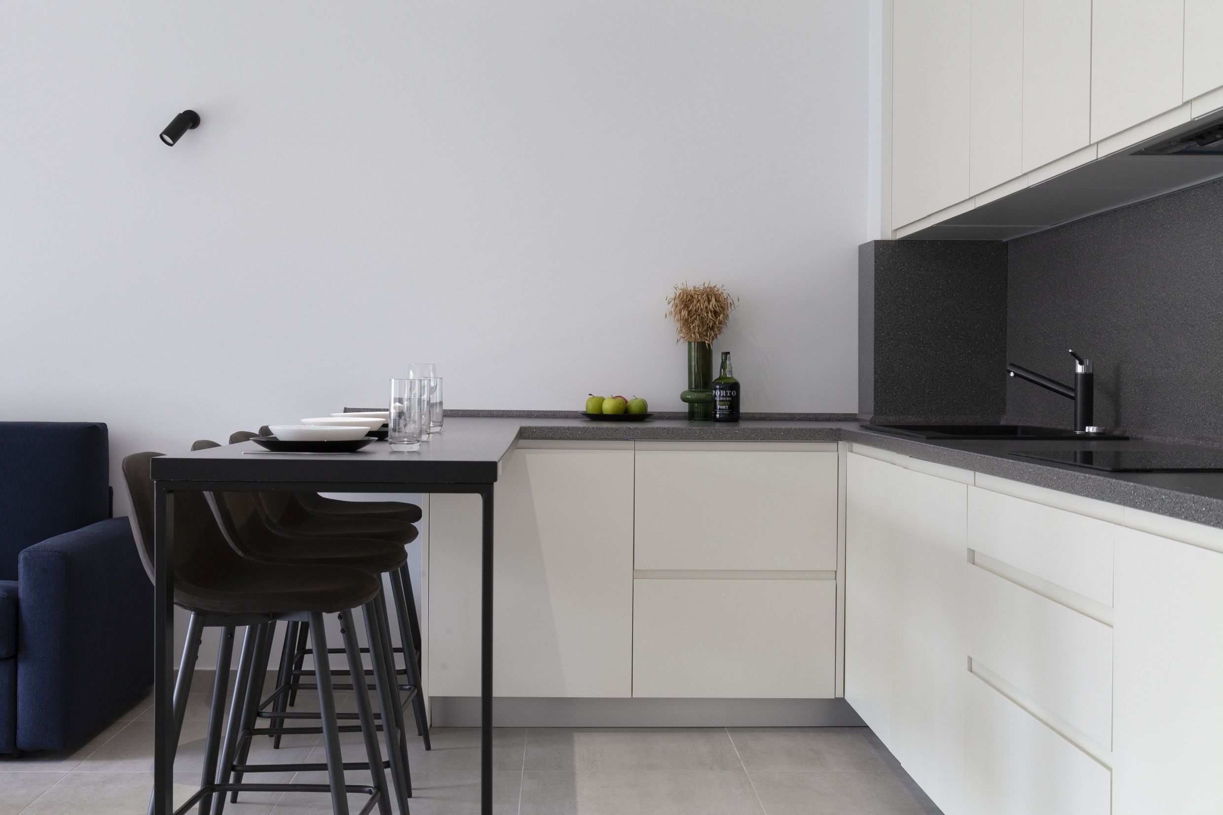 Moderne Küche in einer Wohnung in Kotor, Montenegro: weiße Fronten, dunkle Arbeitsplatte und Bartheke mit Stühlen.