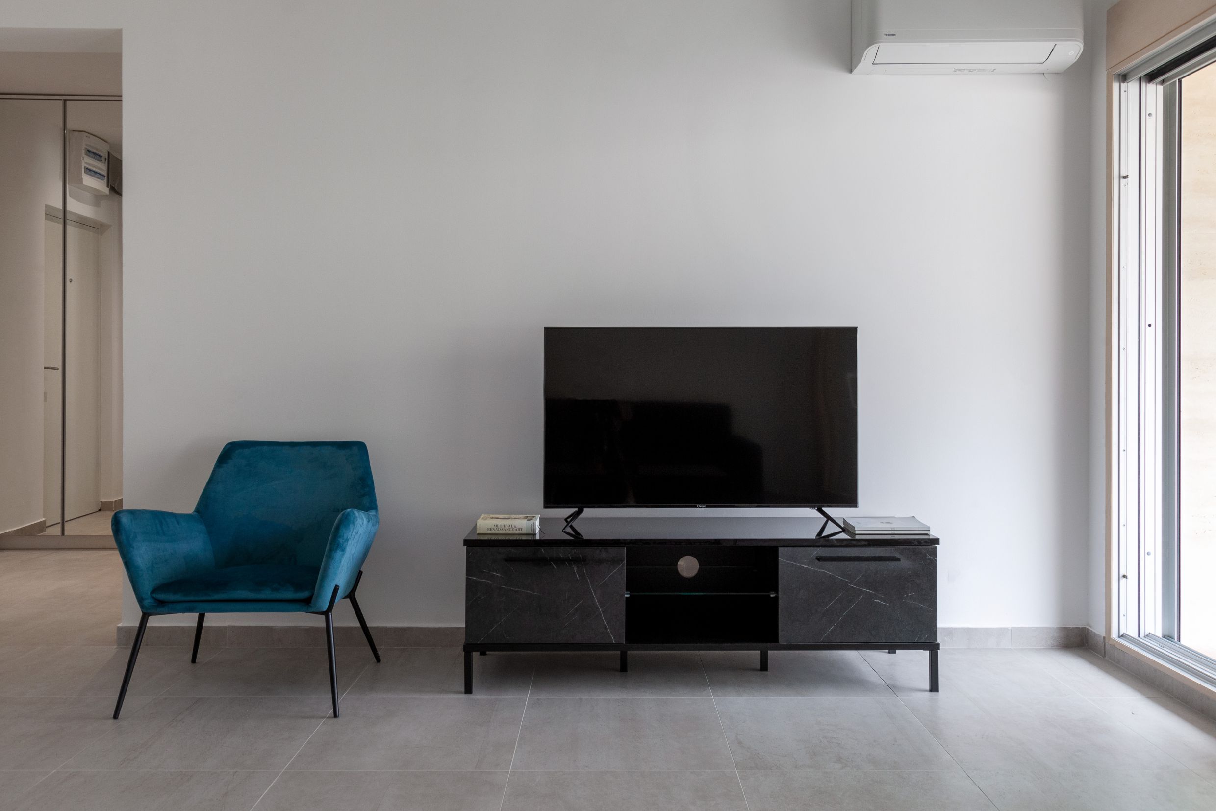 Modernes Wohnzimmer in einer Wohnung in Kotor, Montenegro: blauer Sessel, schwarzes TV-Lowboard und Panoramafenster.