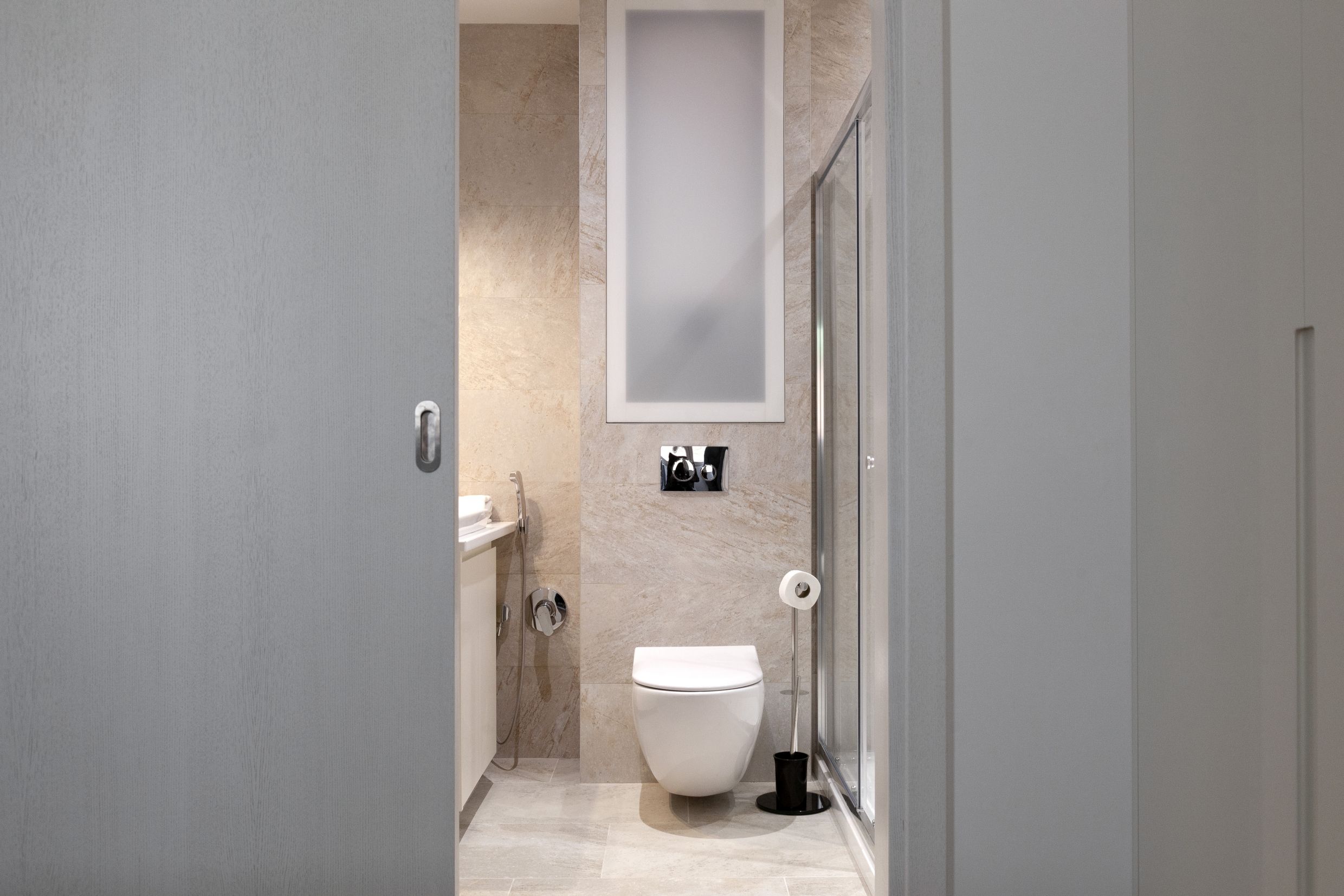 Modernes Badezimmer in einer Wohnung in Kotor, Montenegro: Hänge-WC, Duschkabine und beige Fliesen.