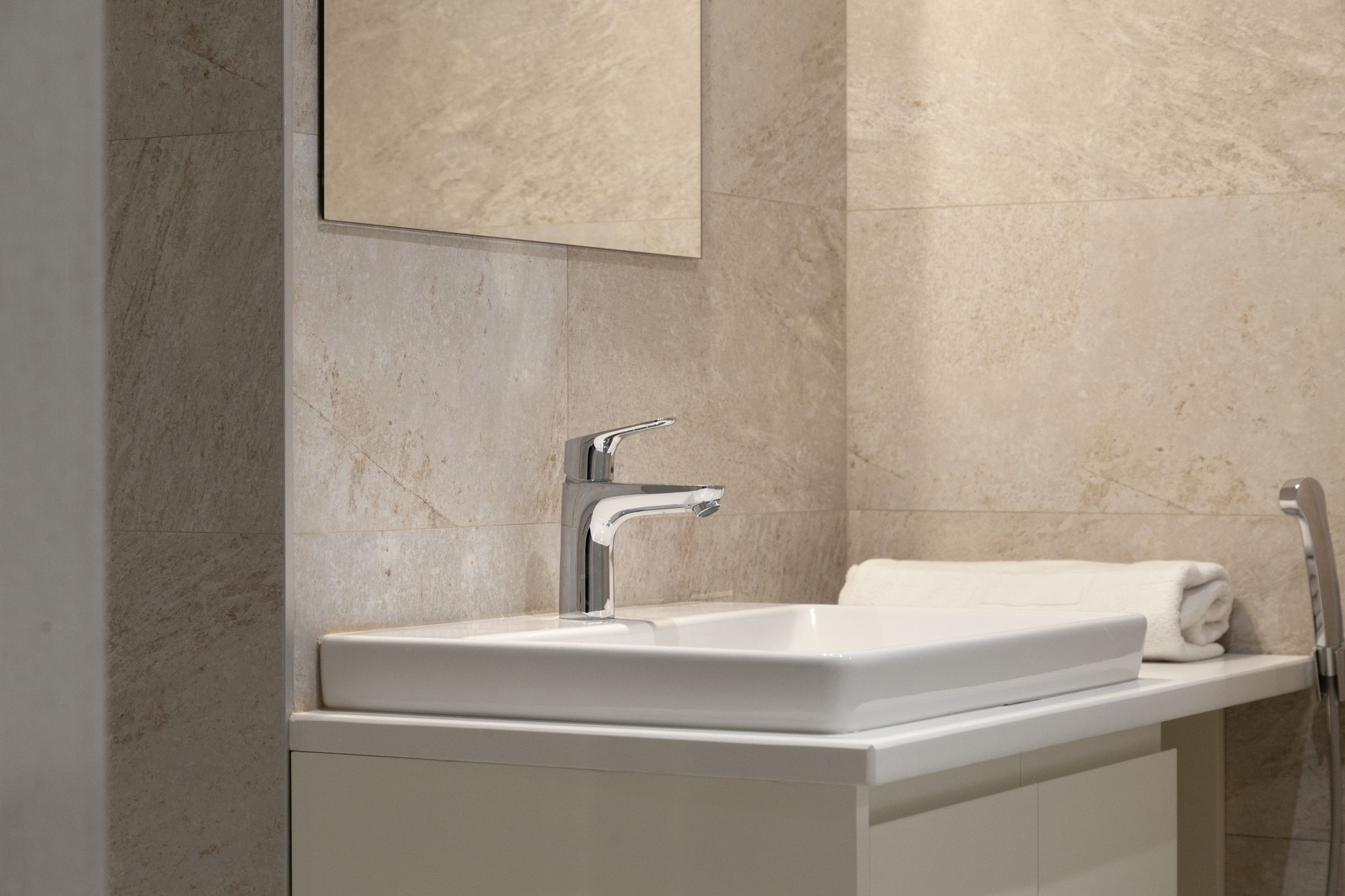 Modernes Badezimmer in einer Wohnung in Kotor, Montenegro: weißes Waschbecken, verchromte Armatur und Steinoptik-Fliesen.