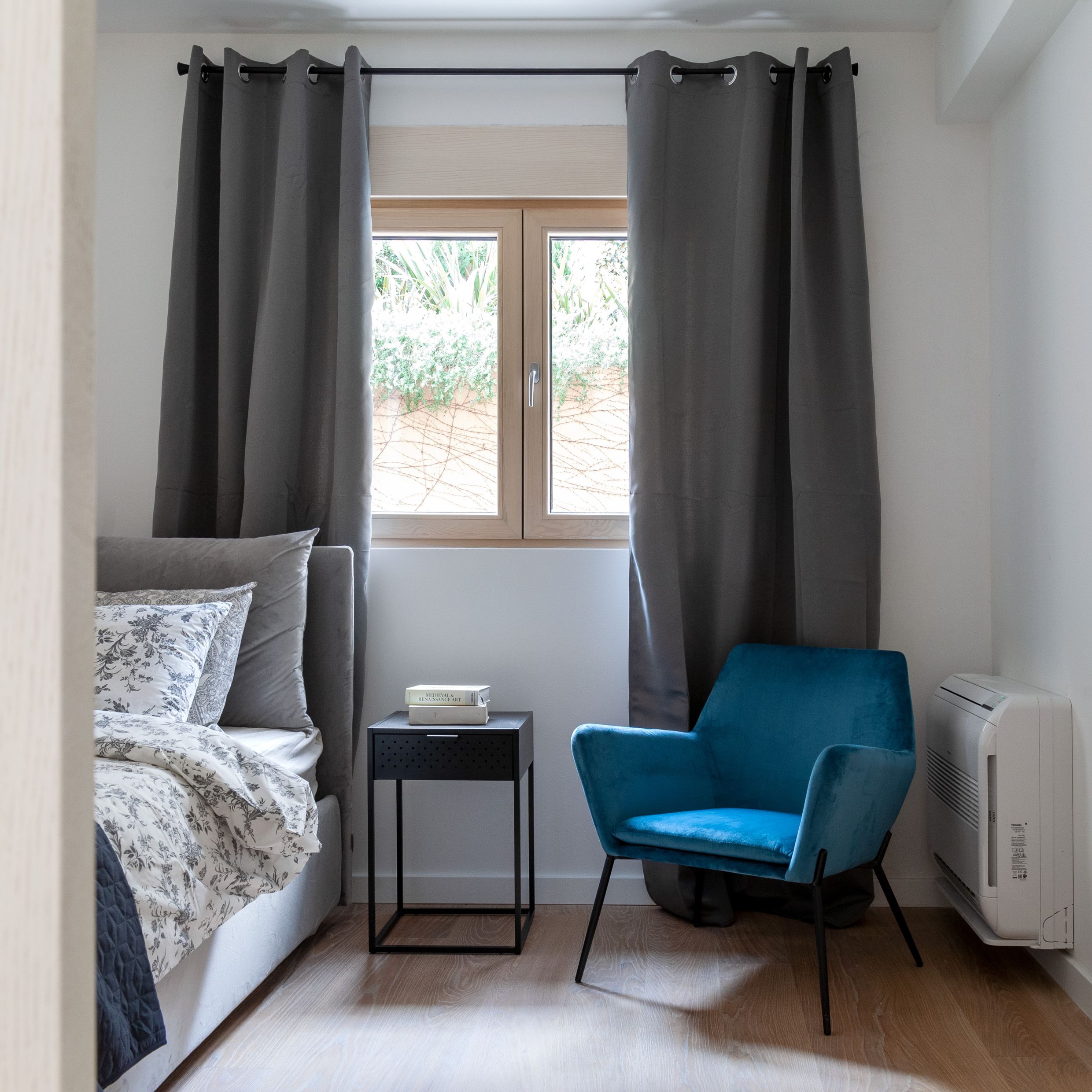 Modernes Schlafzimmer in einer Wohnung in Kotor, Montenegro: graues Bett, blauer Sessel, Nachttisch und Blick aus dem Fenster.