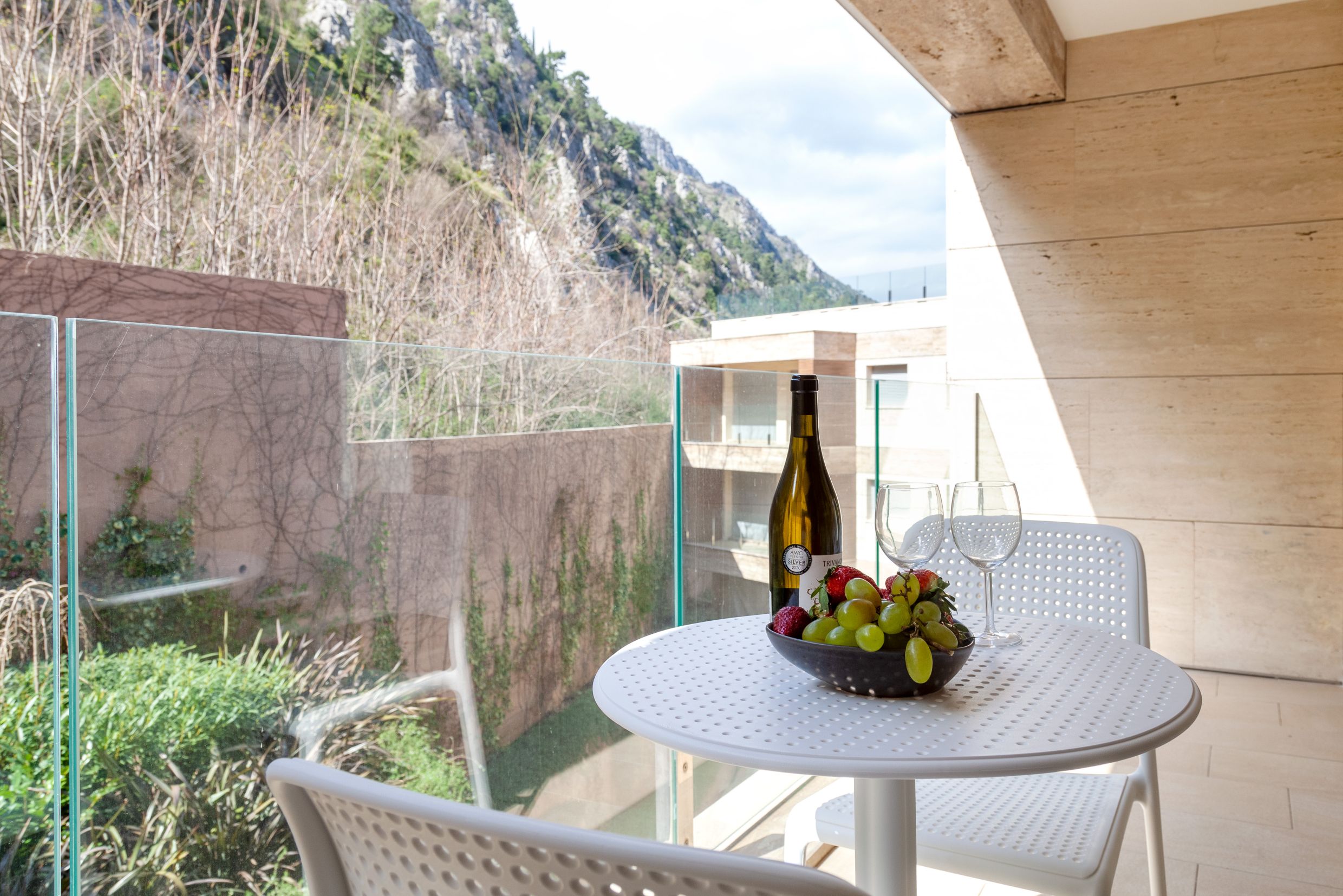 Balkon einer Wohnung in Kotor, Montenegro: weißer Tisch mit Wein und Obst, Panoramablick auf die Berge und moderne Ausstattung.