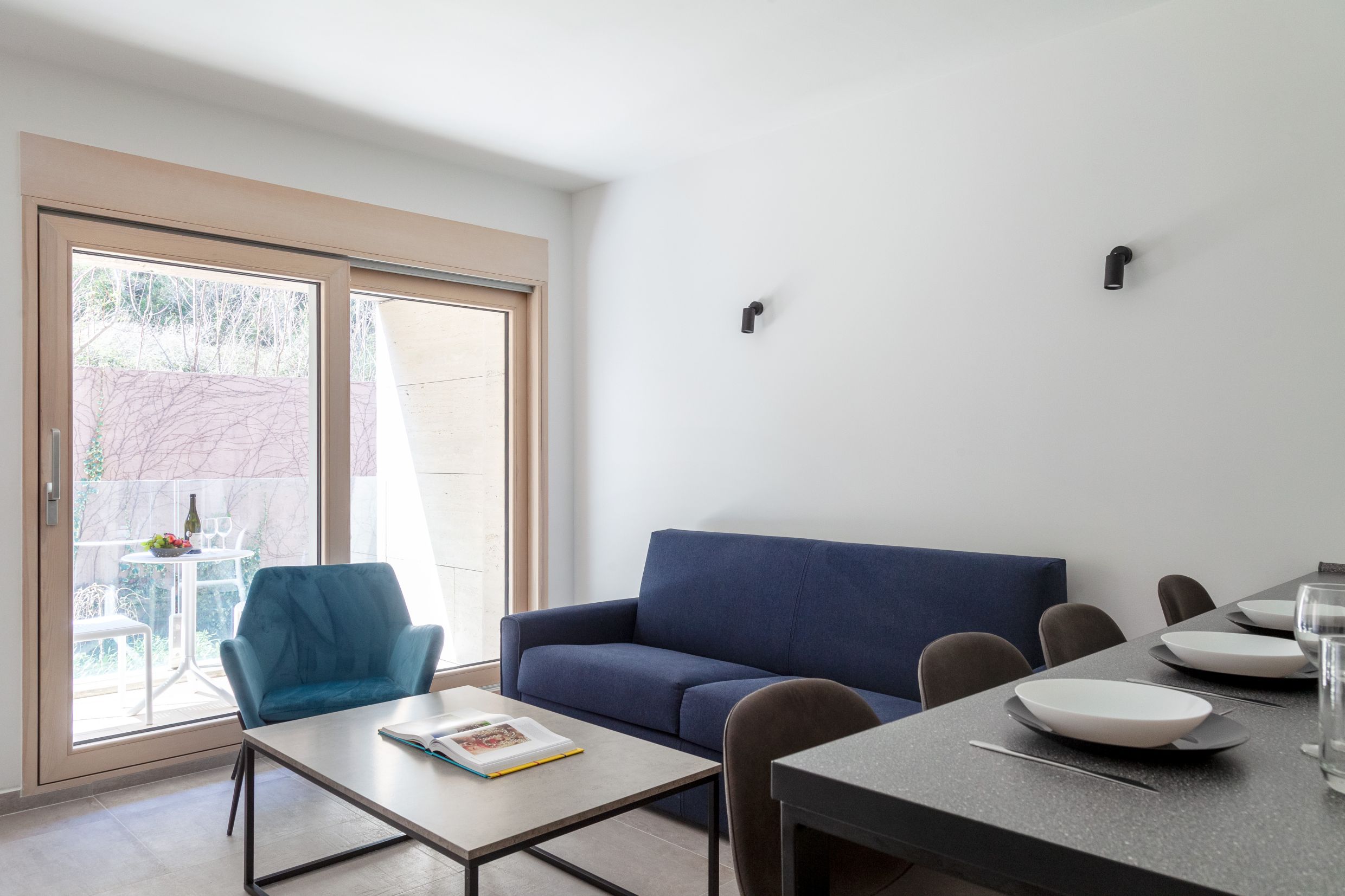 Modernes Wohnzimmer in einer Wohnung in Kotor, Montenegro: blaues Sofa, Sessel, Essbereich und Zugang zur Terrasse.