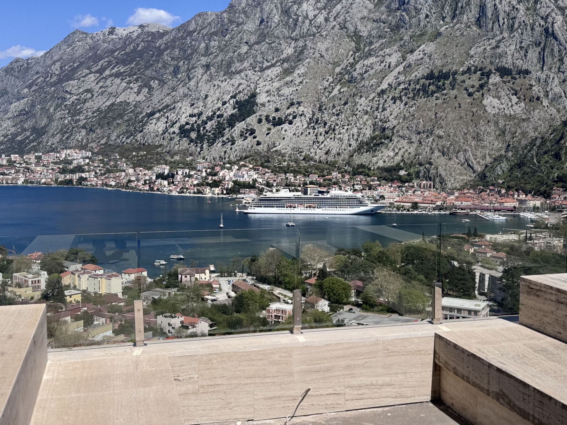Panoramski pogled na Bokokotorski zaliv i planine sa terase stana u Kotoru, Crna Gora, sa staklenom ogradom.