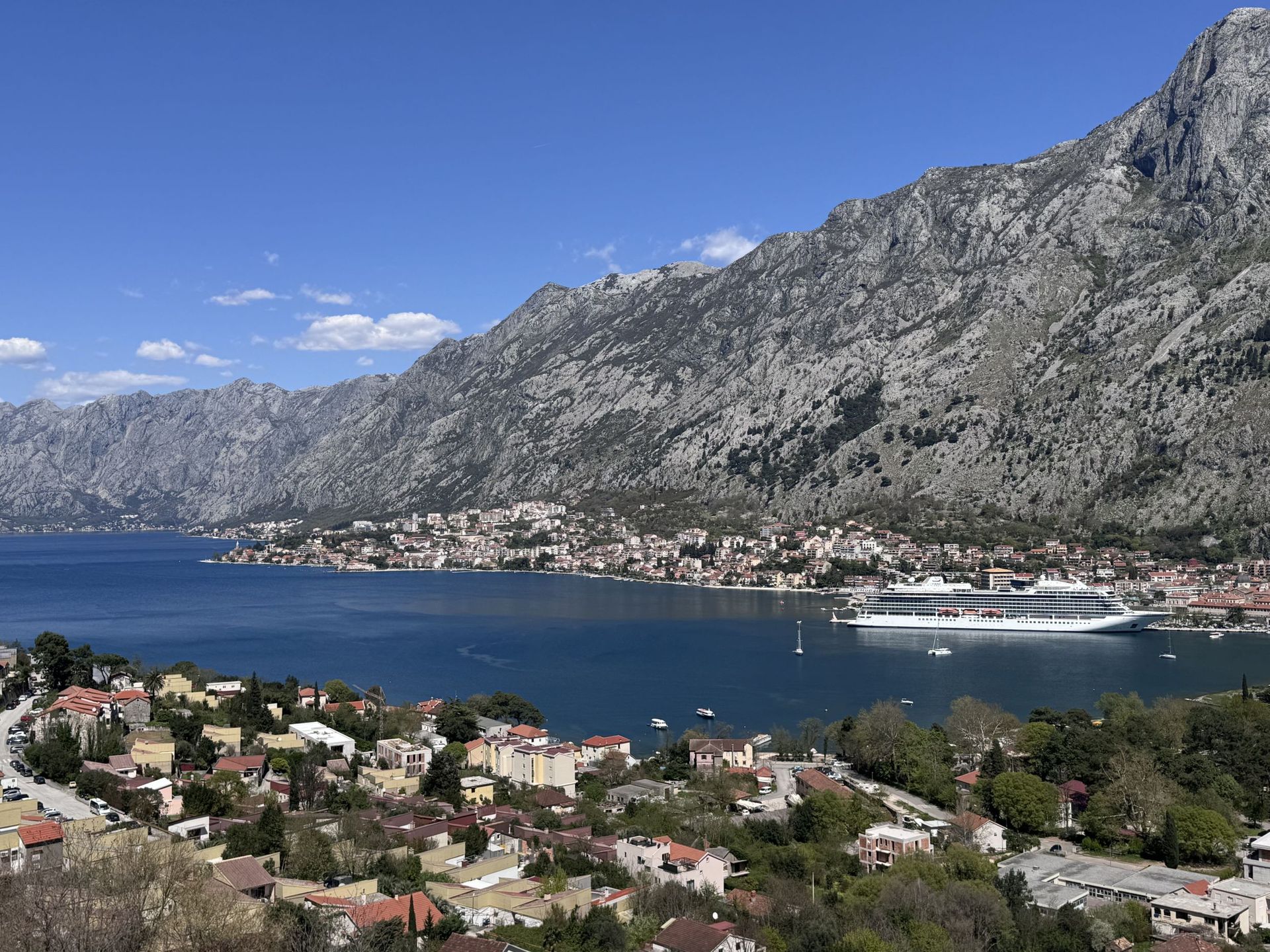 Panoramski pogled na Bokokotorski zaliv i planine iz stana u Kotoru, Crna Gora: more, kruzer i gradska izgradnja.
