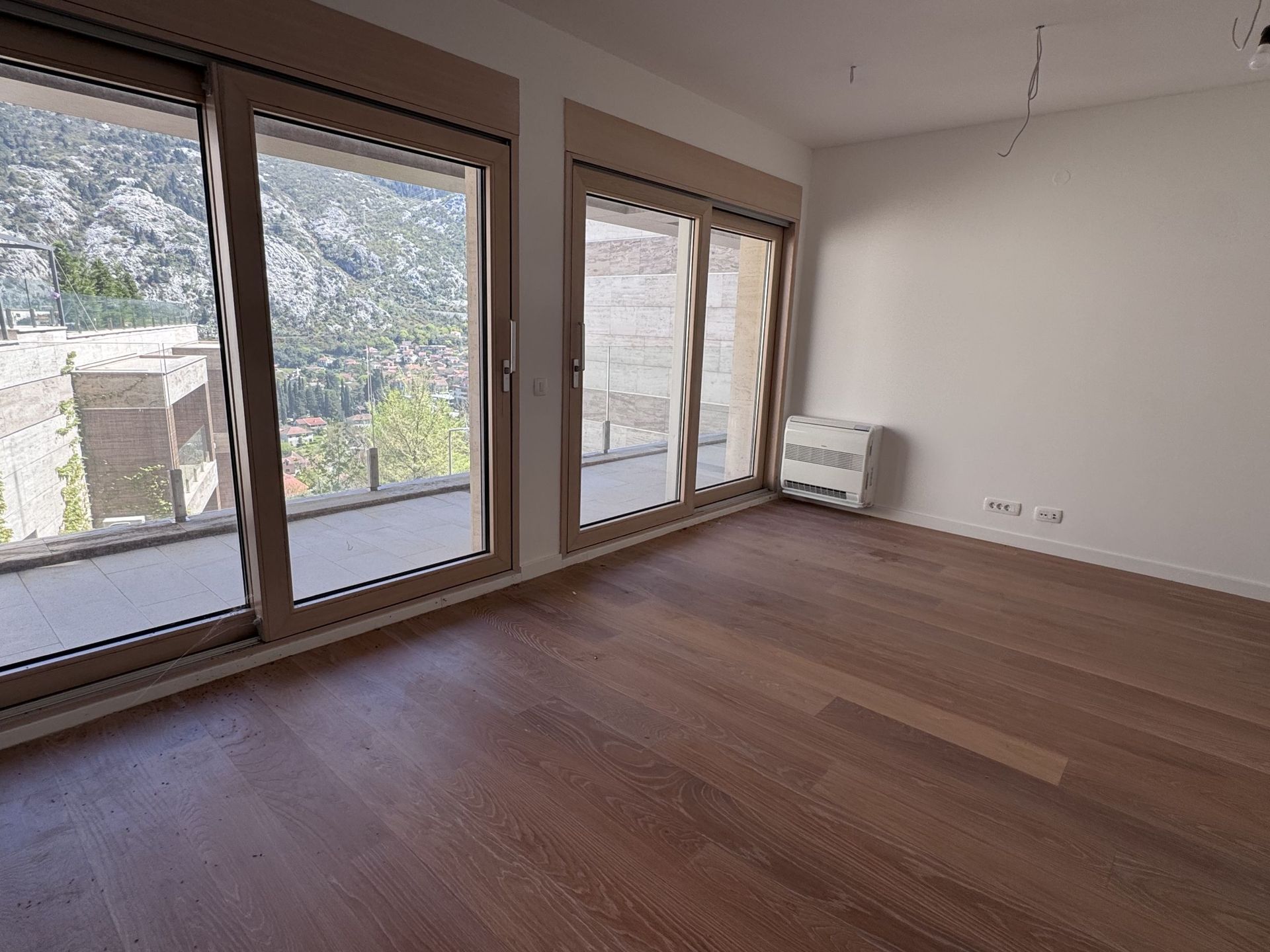 Svetao dnevni boravak u stanu u Kotoru, Crna Gora: panoramski prozori, pogled na planine, parket i izlaz na terasu.